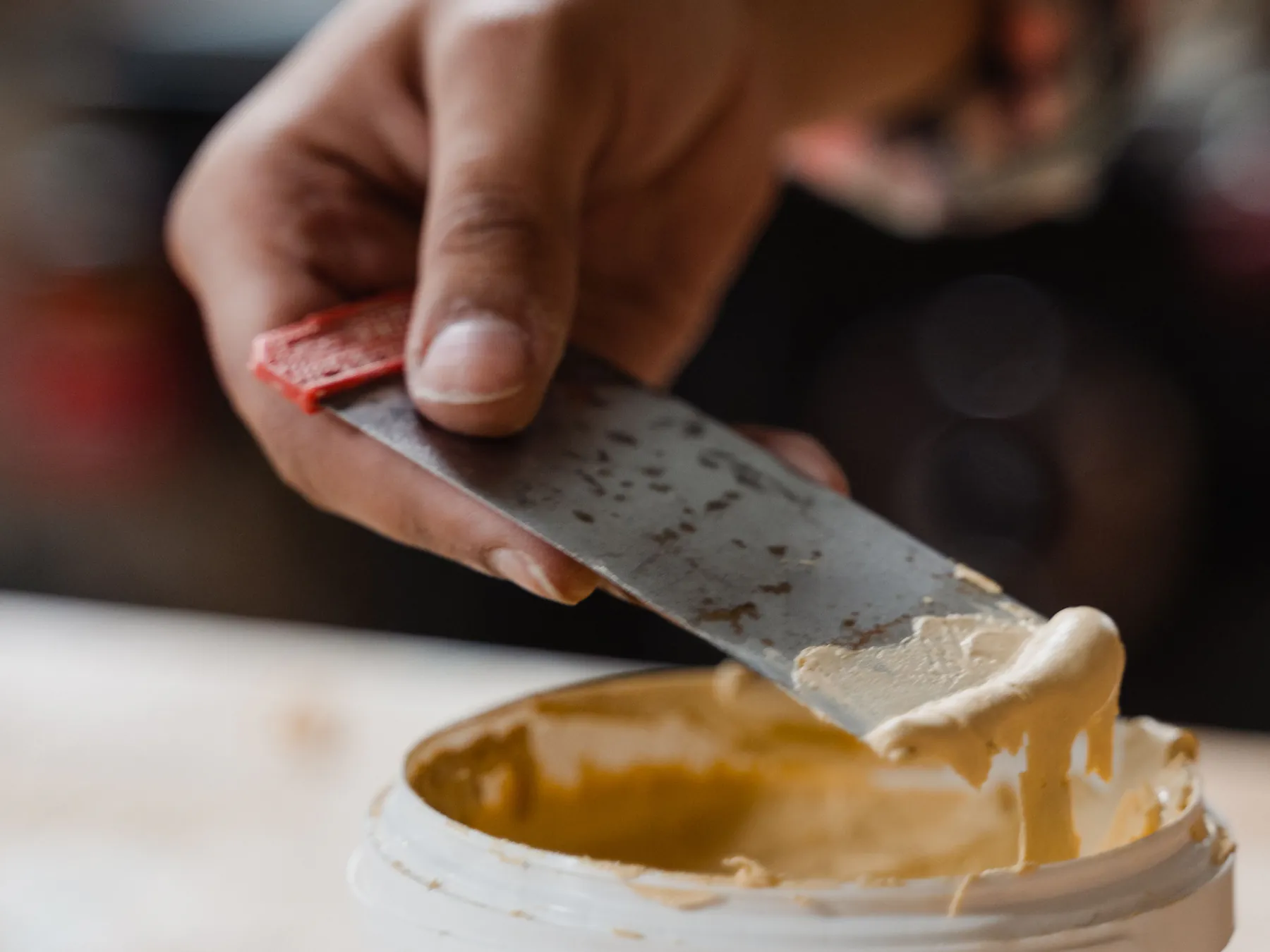 A hand lifting wood filler from an open tub on a putty knife