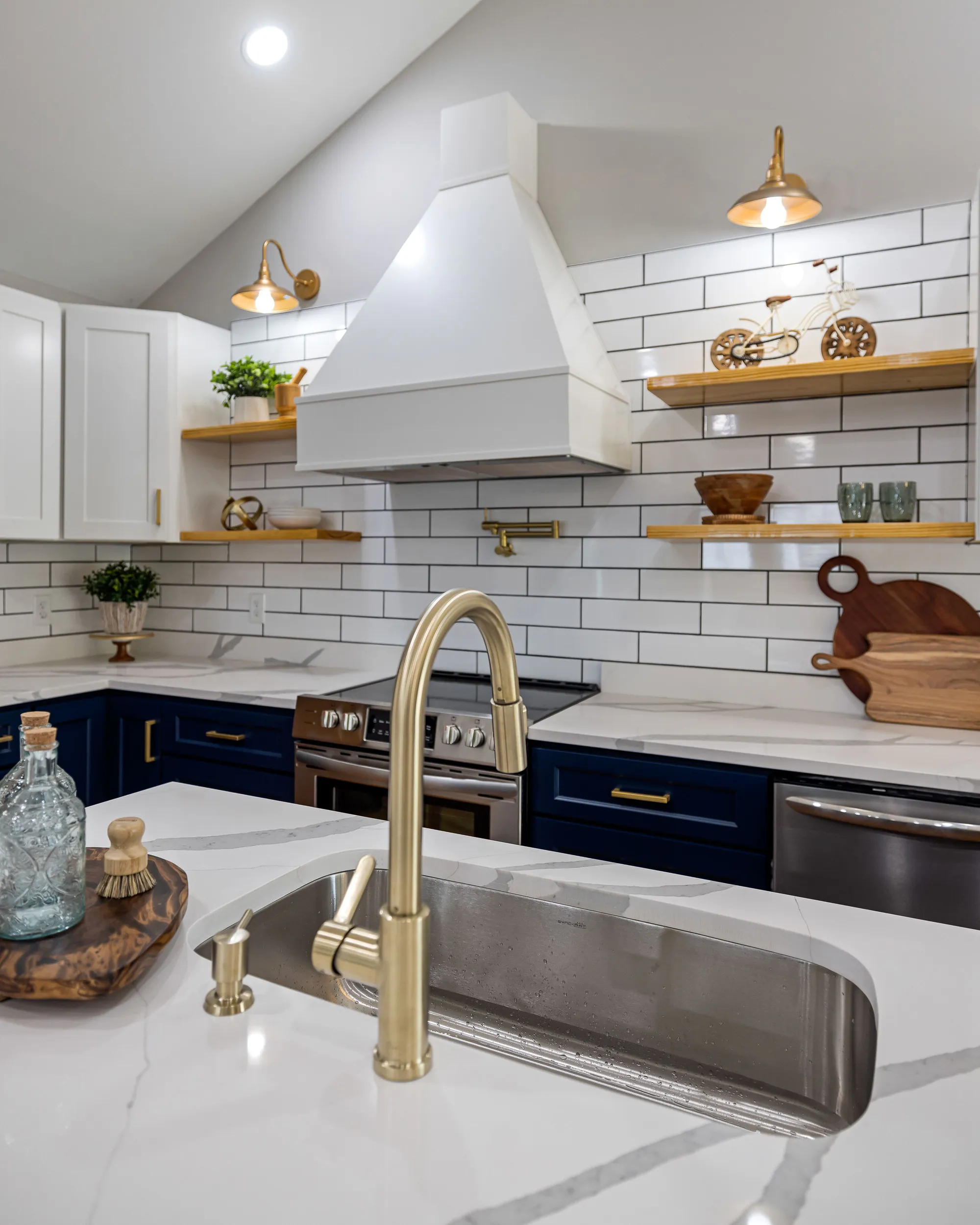 A brass faucet over a white marble island in a kitchen with navy lower cabinets and white subway tile