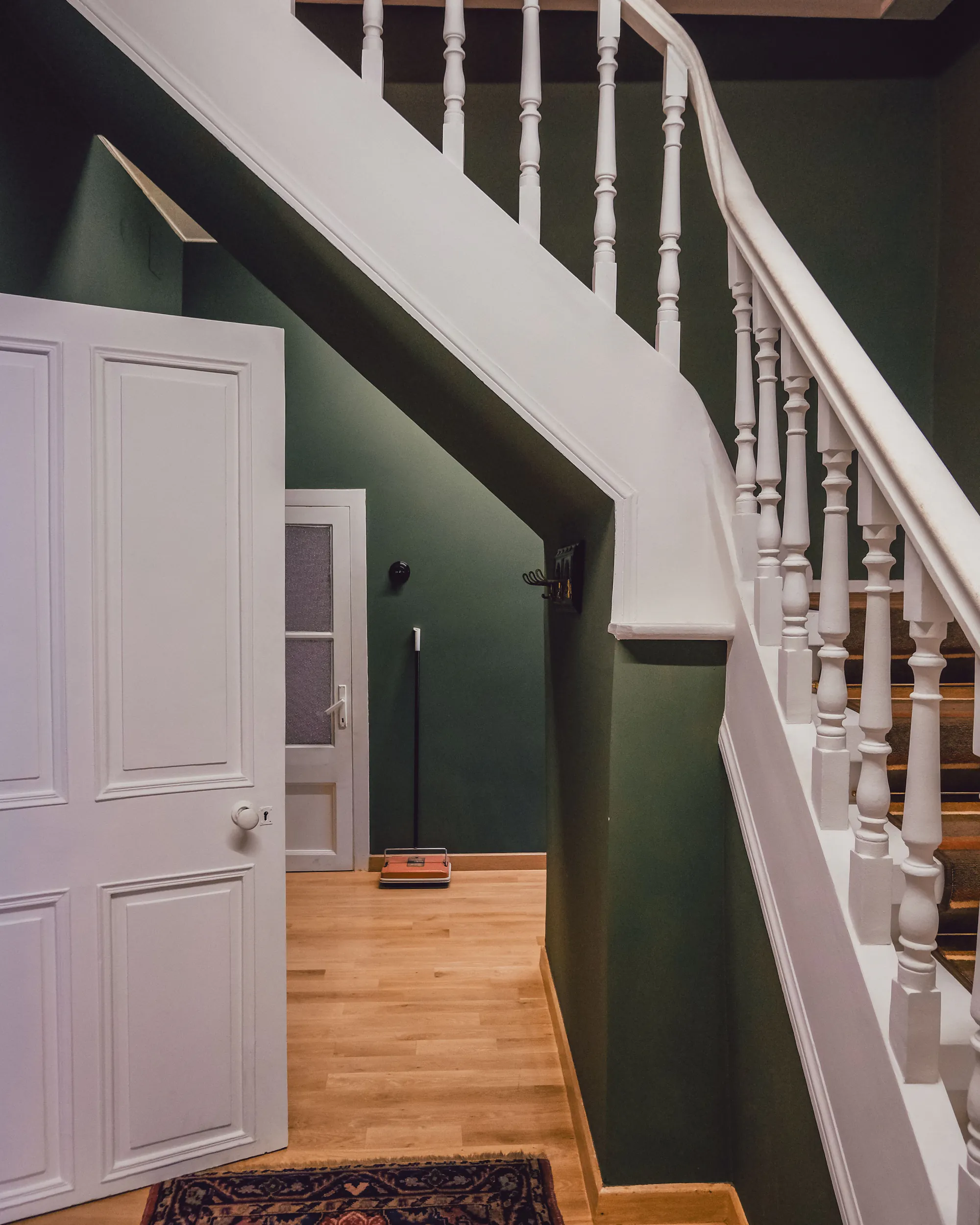 A staircase with white turned balusters and a white-painted stringer against deep green walls