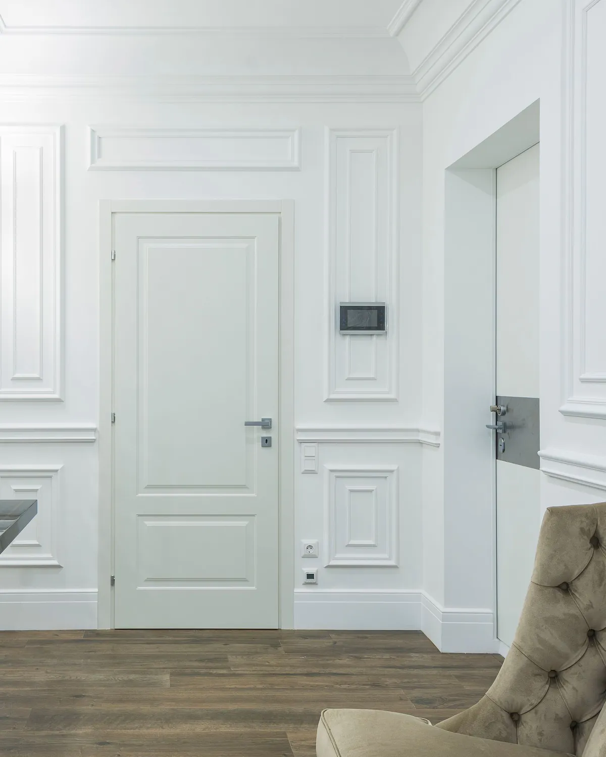A white hallway with applied panel mouldings, a crown cornice and a panelled door