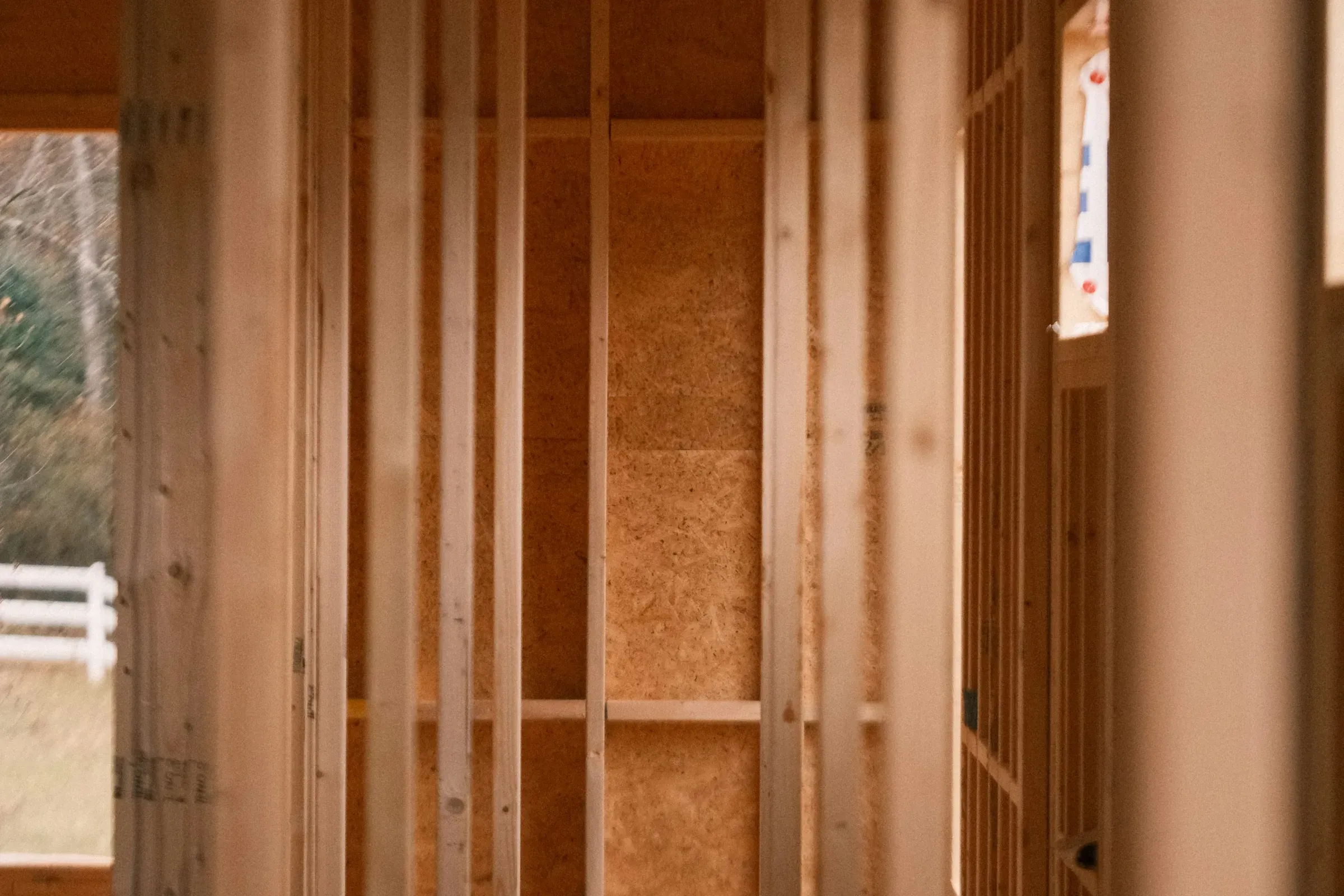 Rows of new wood studs and blocking inside a framed room, with sheathing behind them