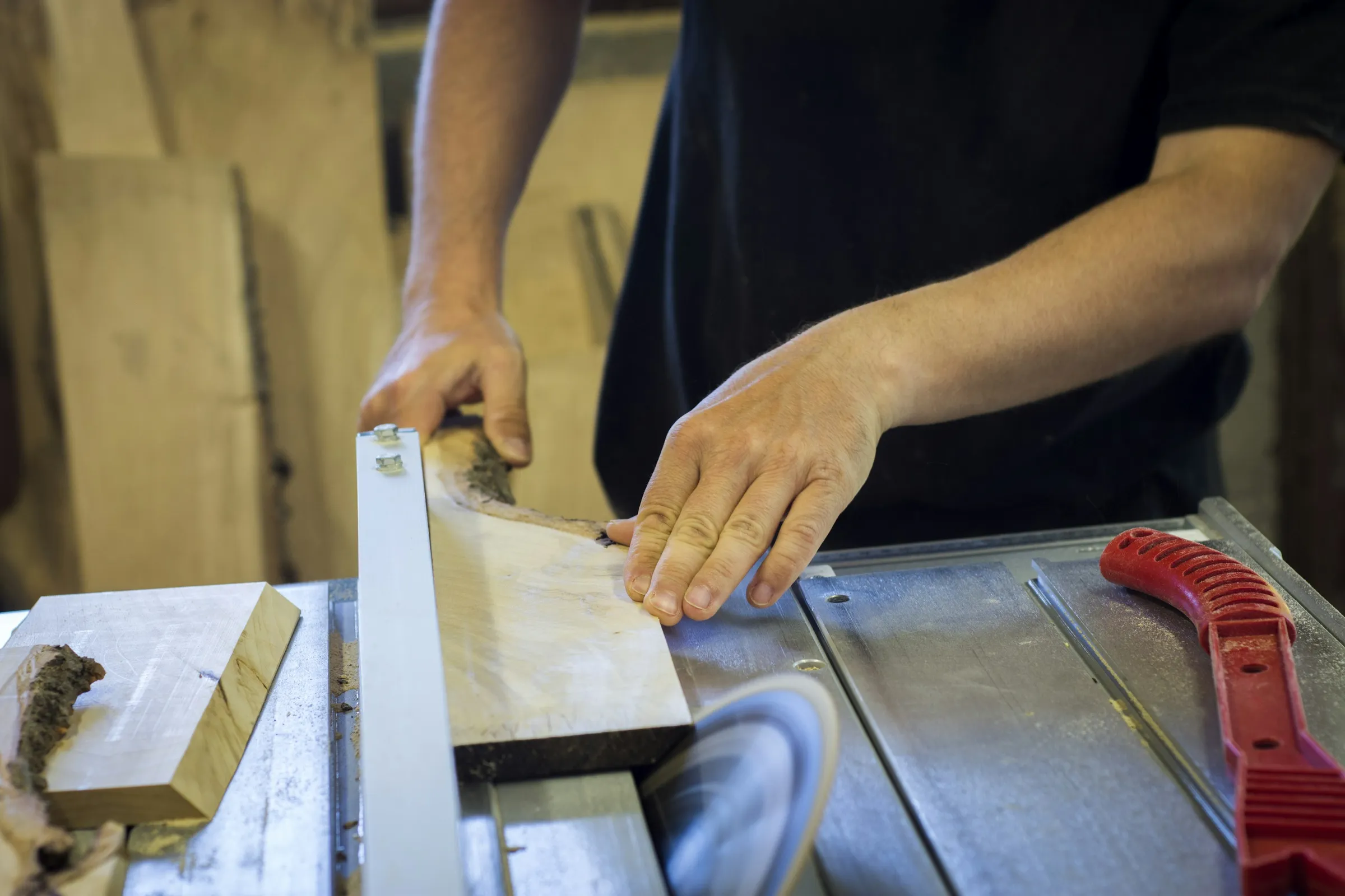 Two hands guiding a wooden board along the fence of a table saw in a woodshop