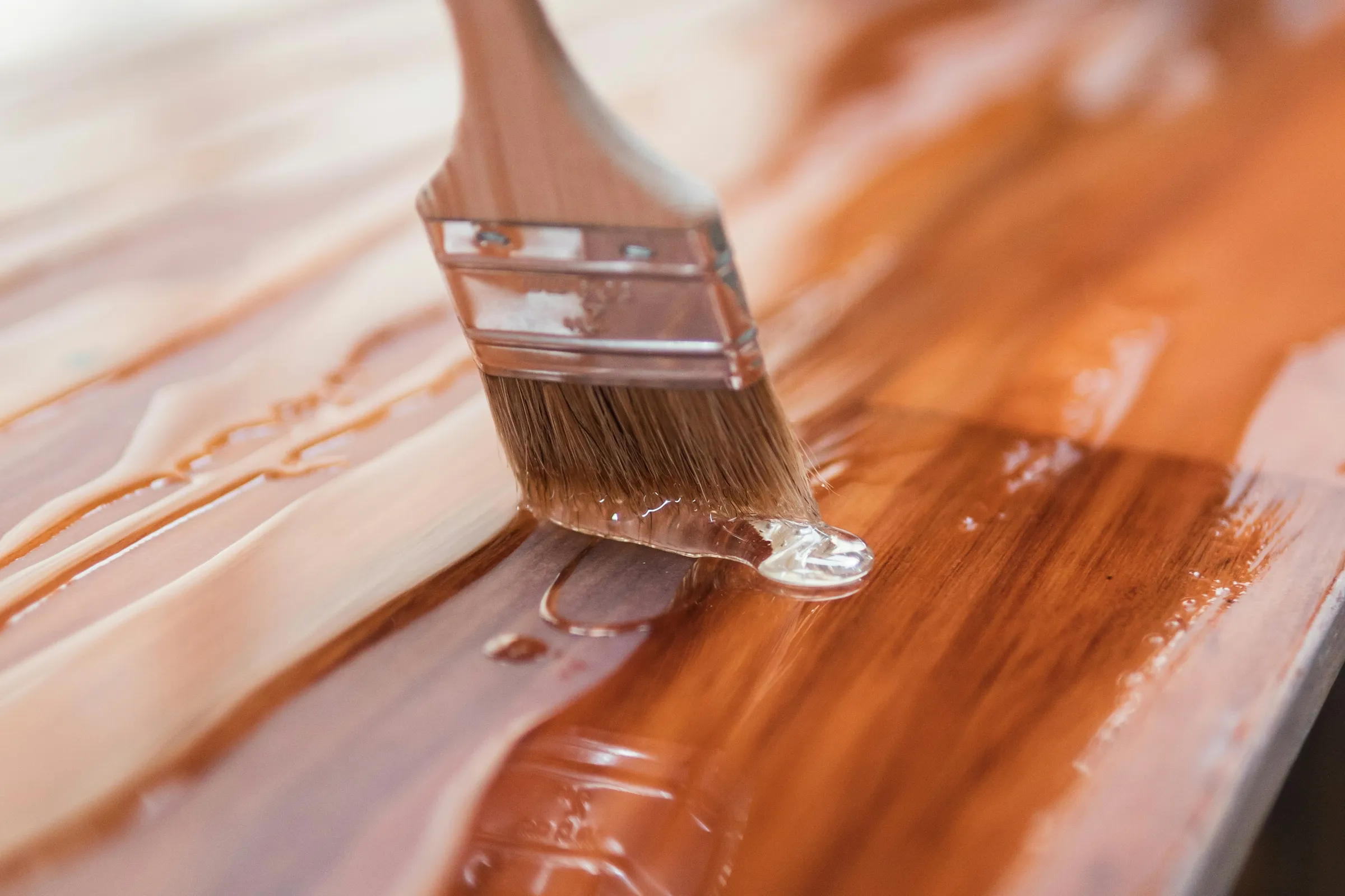 A hand drawing a brush through a glossy coat of amber finish on a wooden board
