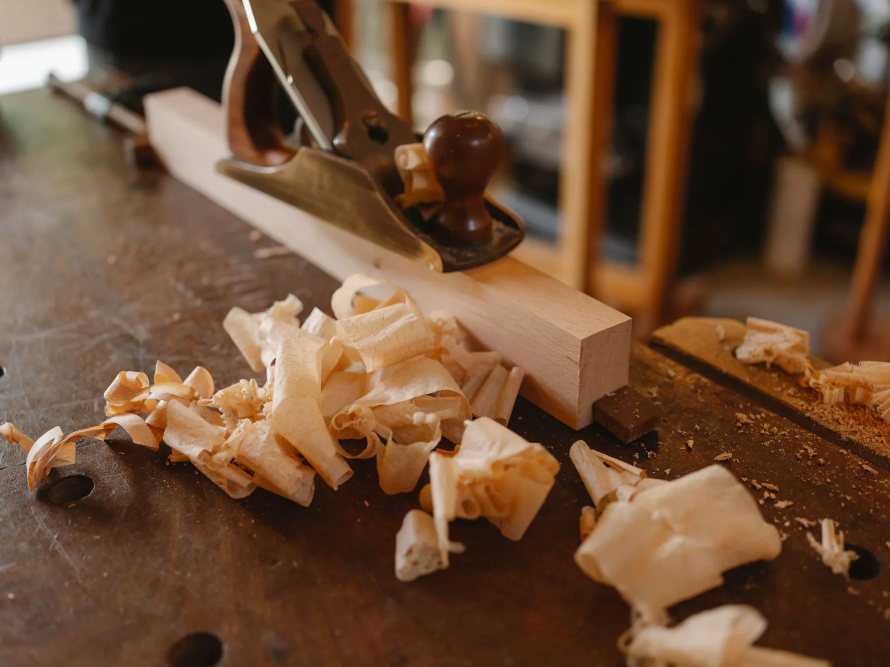 A hand plane resting on a pale wooden board among curled shavings on a workbench