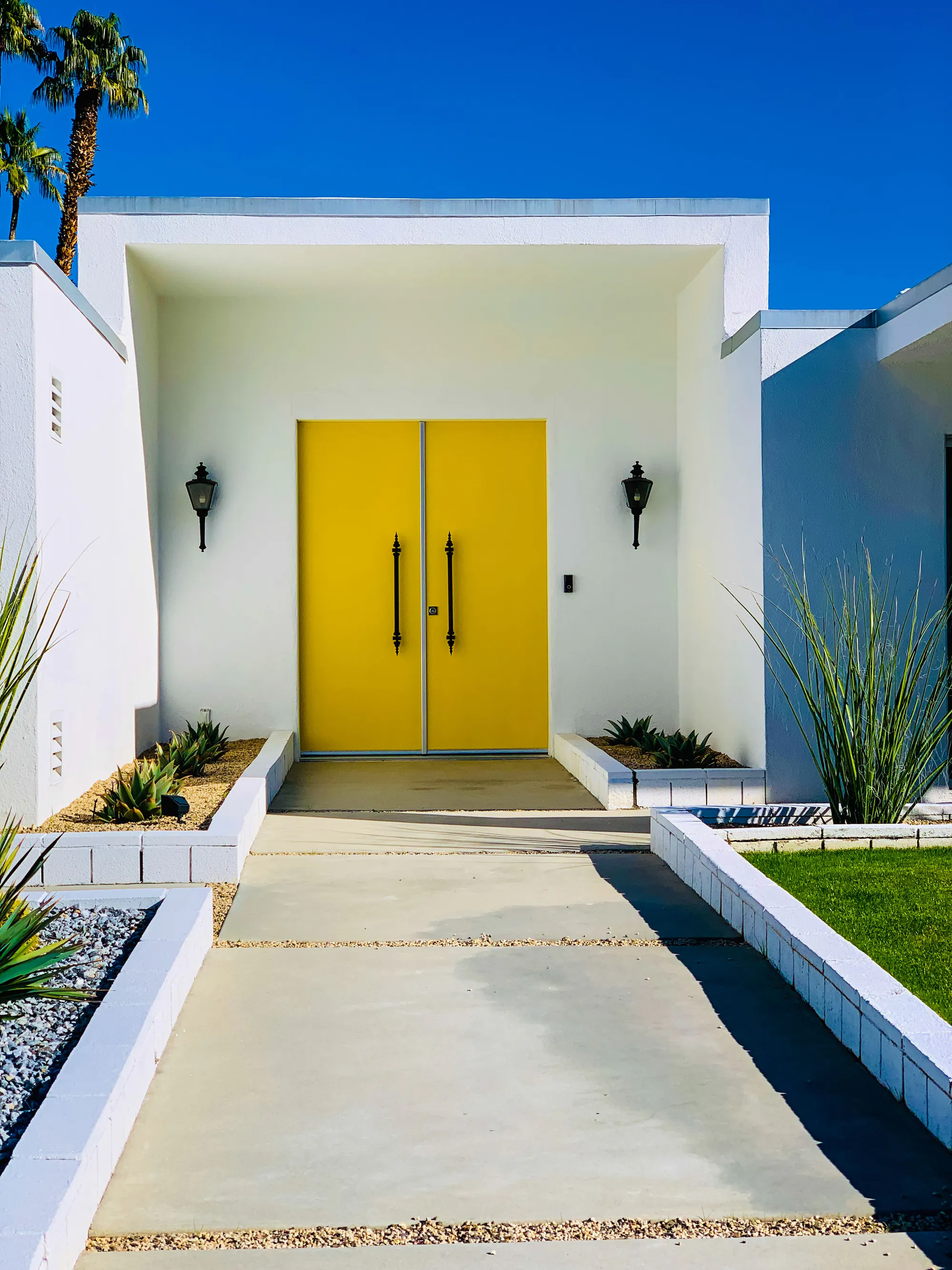 A white modern entry with double yellow doors at the end of a concrete walk