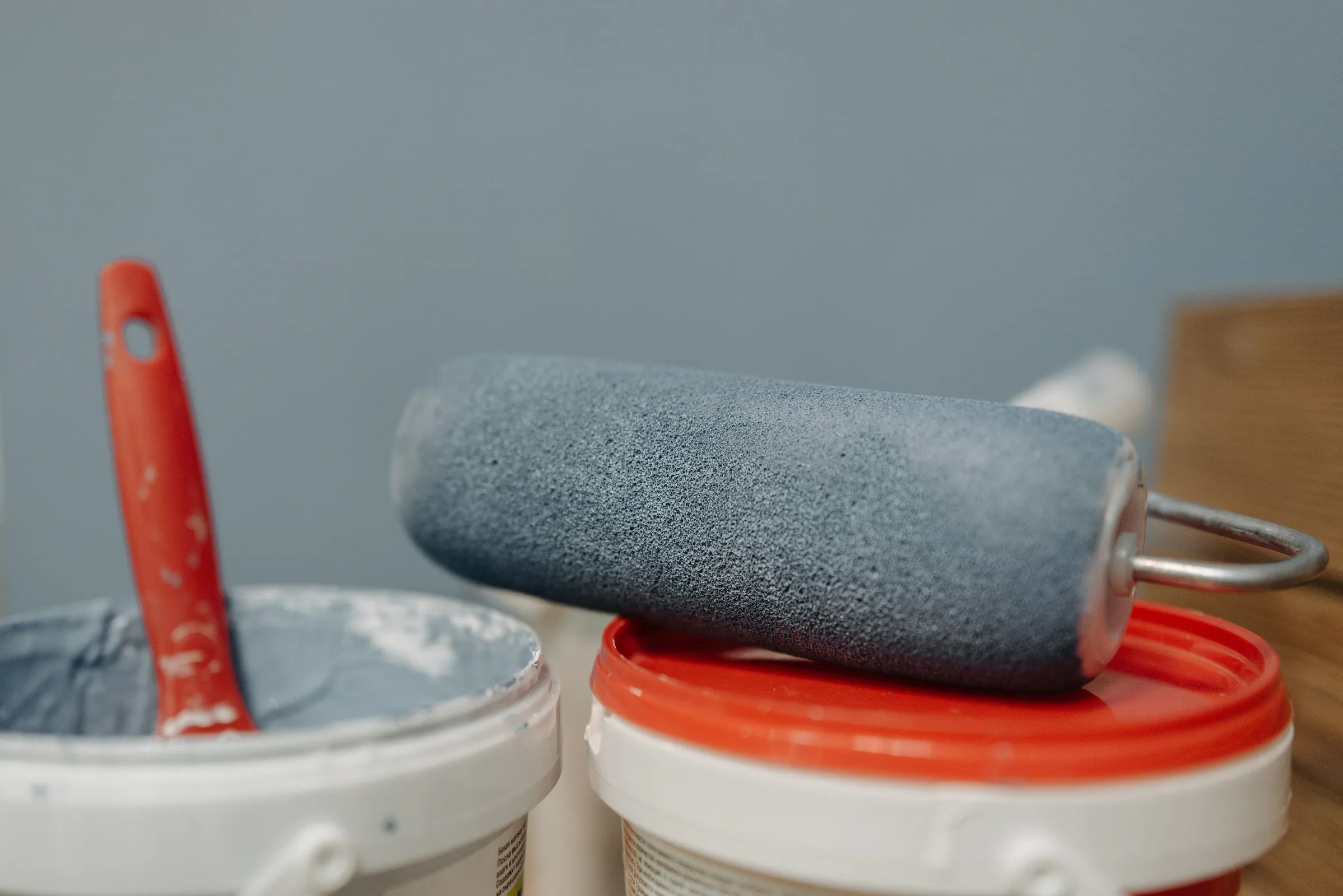 A paint roller resting on two open pails of gray-blue paint