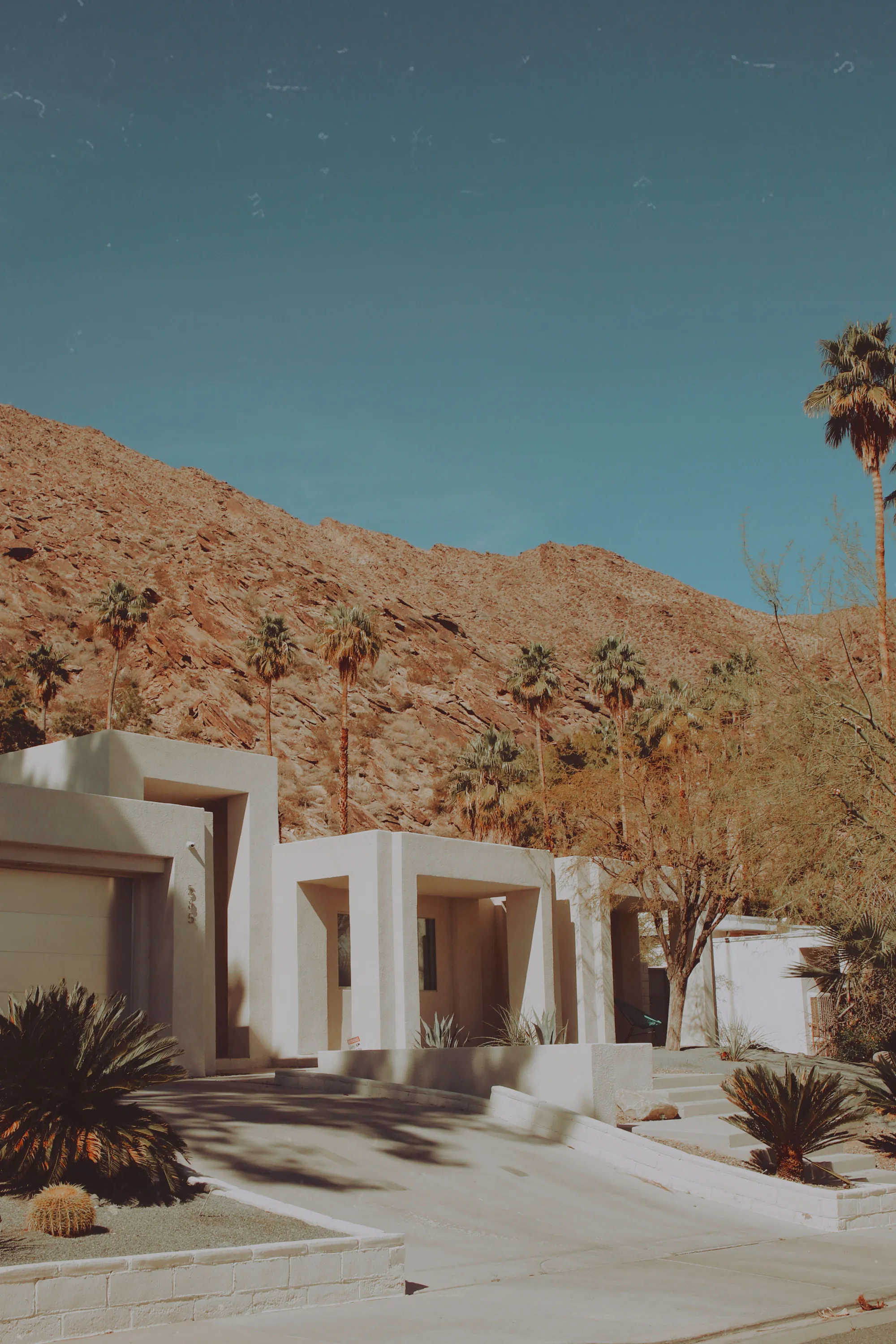 A white modern desert house below a rocky hill under a clear blue sky