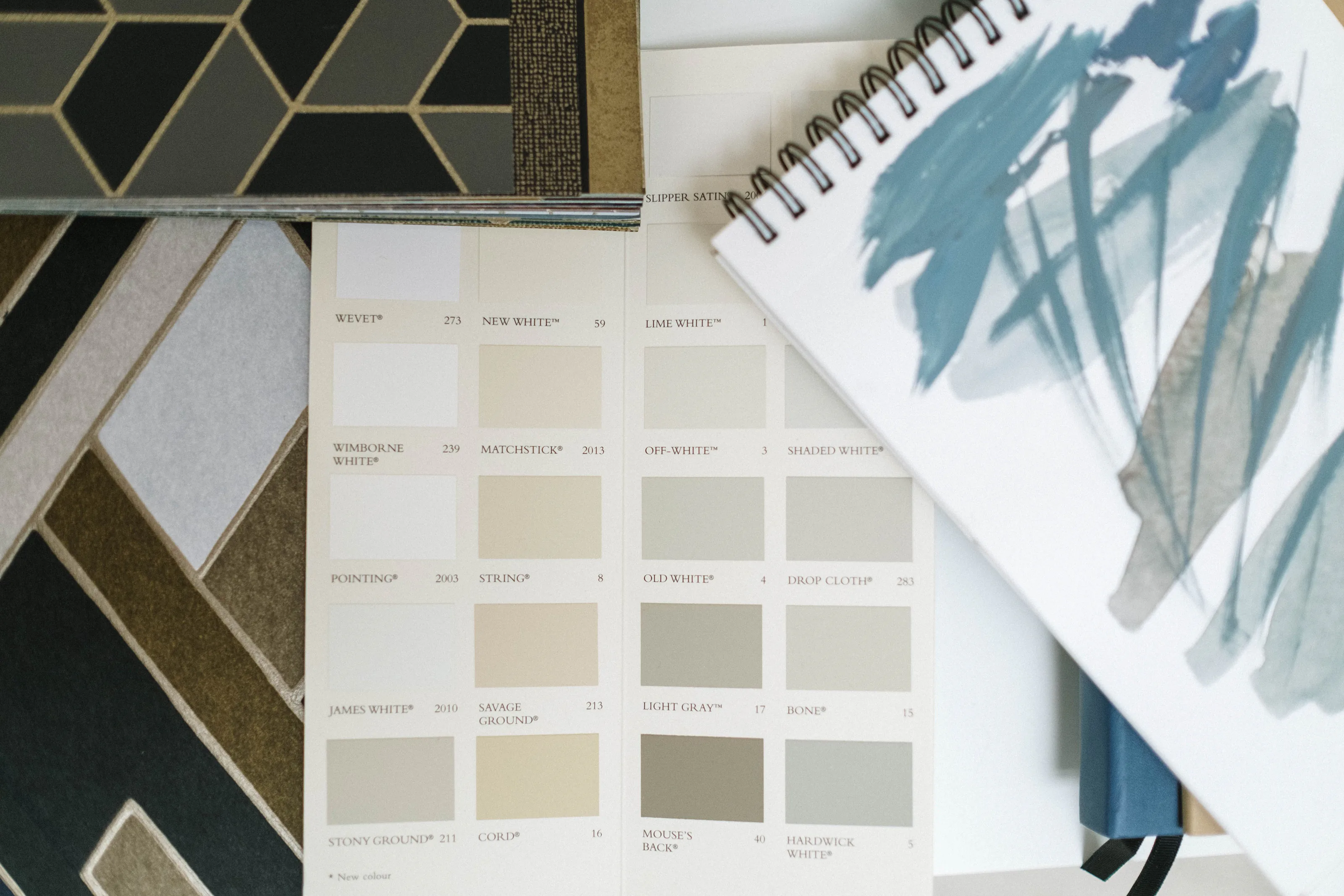 Neutral paint color cards and a sketchbook laid over navy and gold patterned tiles