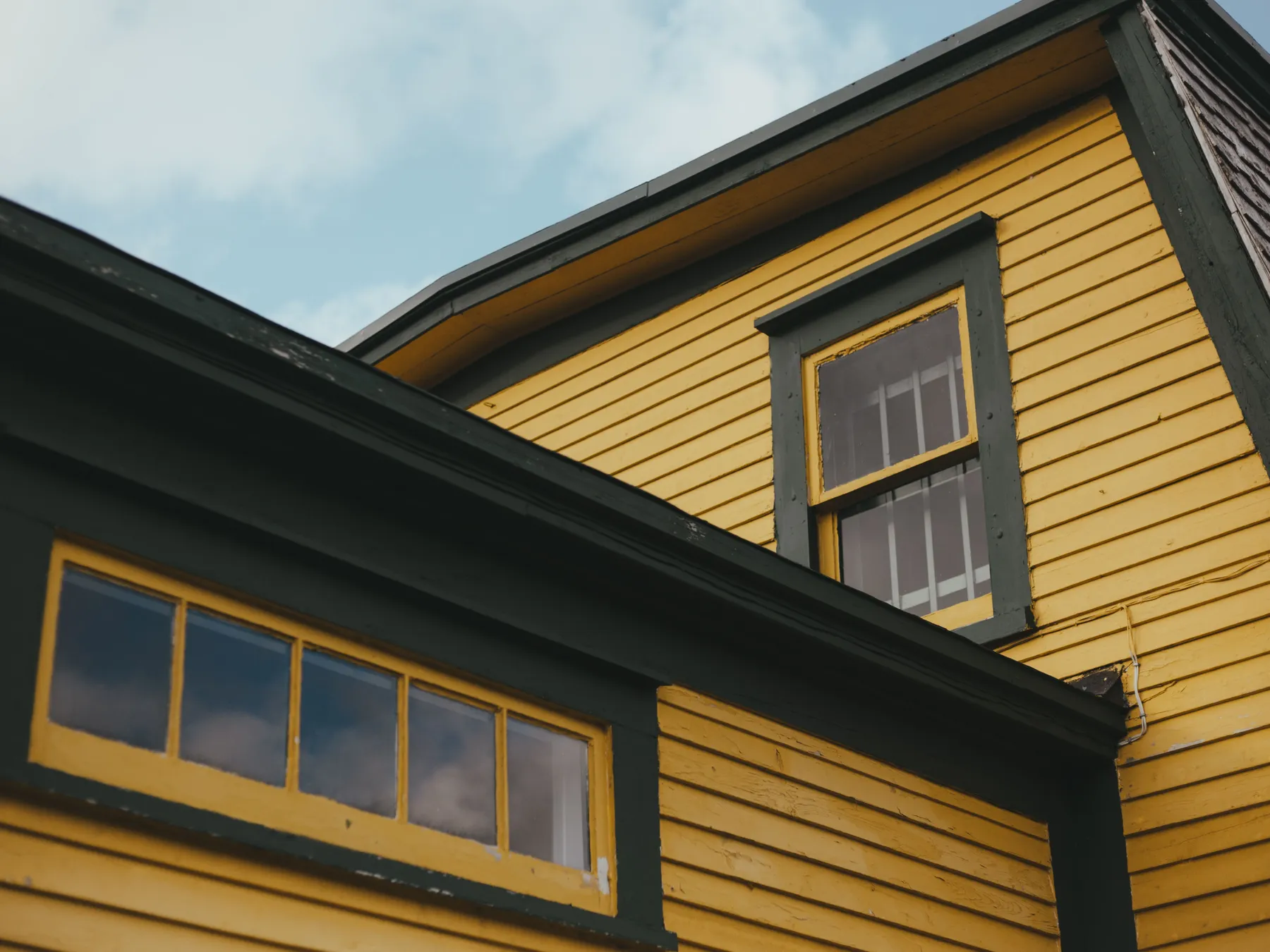 Yellow clapboard siding with dark green window trim under a blue sky