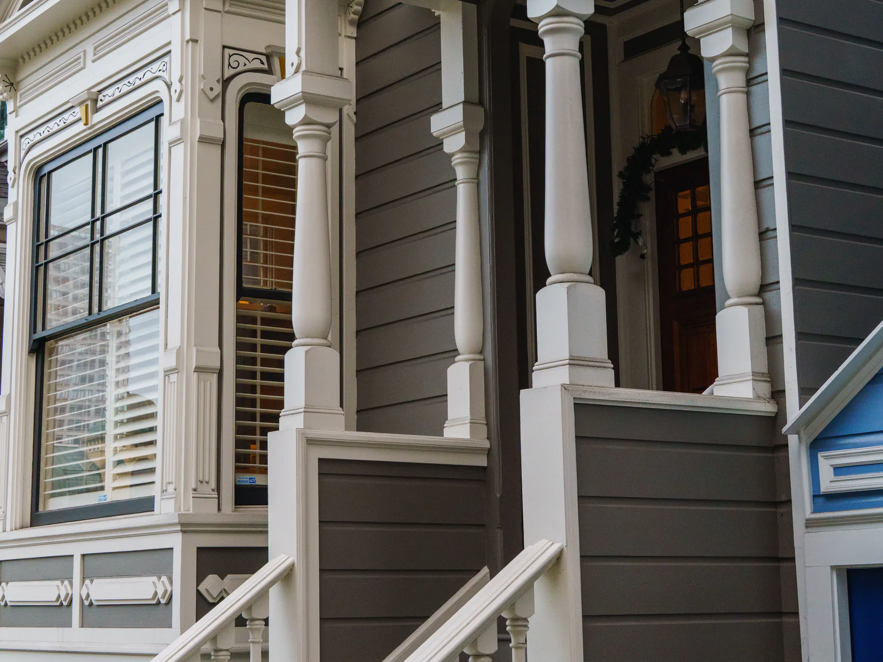 A Victorian entry porch with white turned columns and railings against grey-brown siding