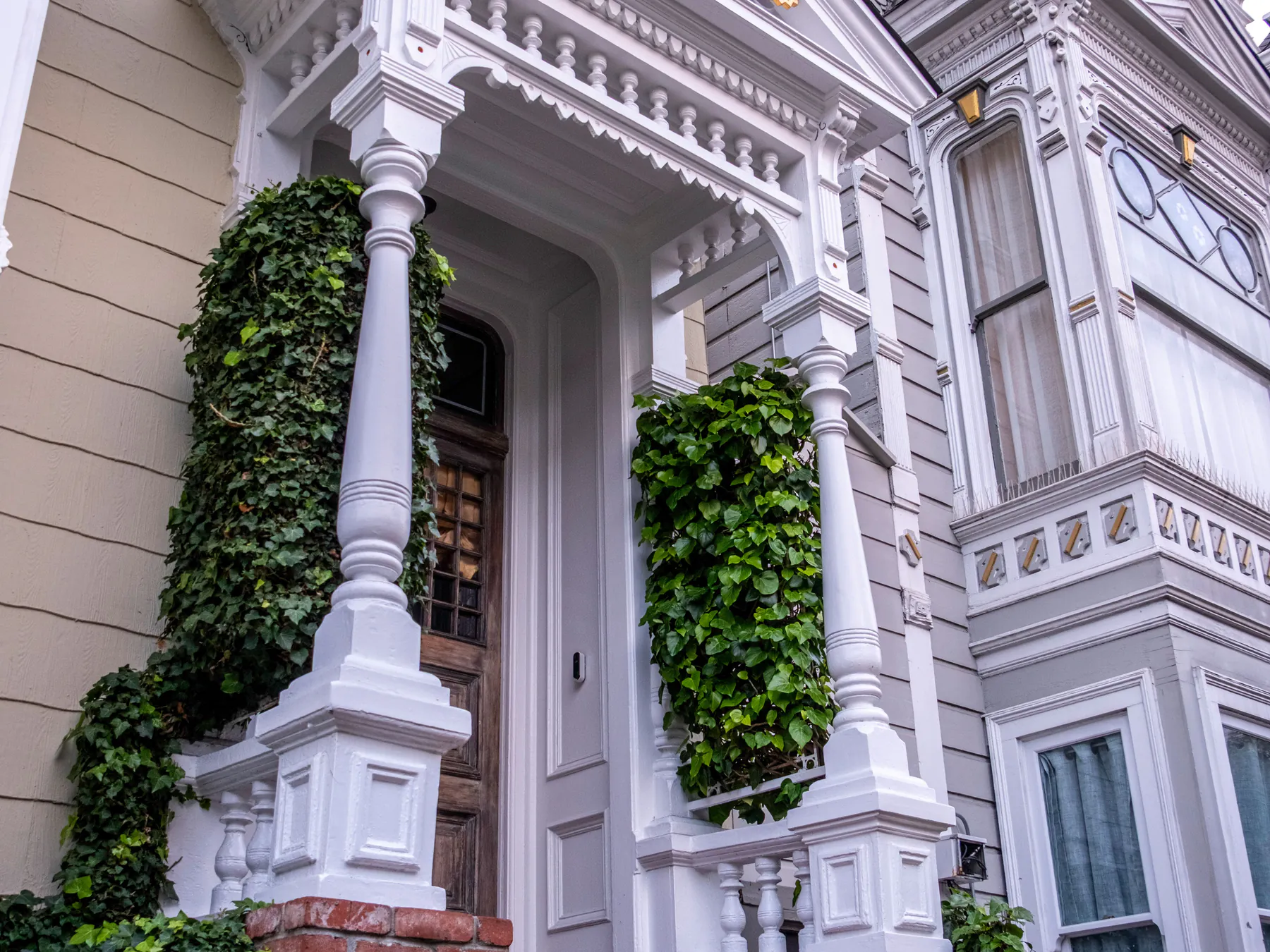 A Victorian entrance with white carved columns and pediment, climbing ivy and red brick steps