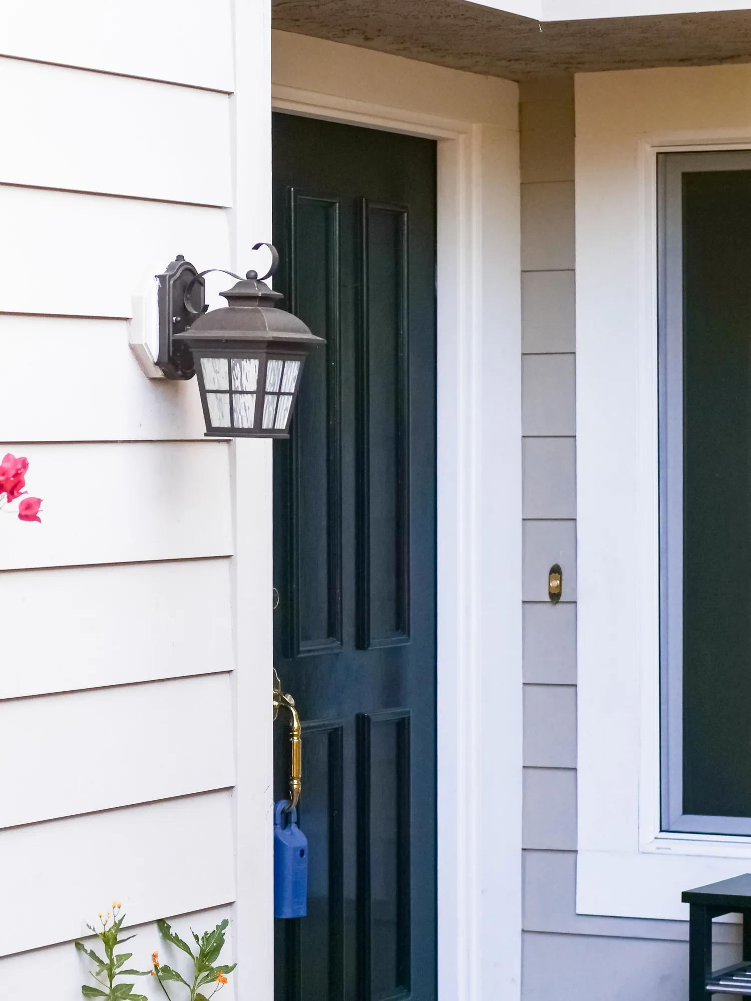A dark green front door beside a black lantern on white lap siding