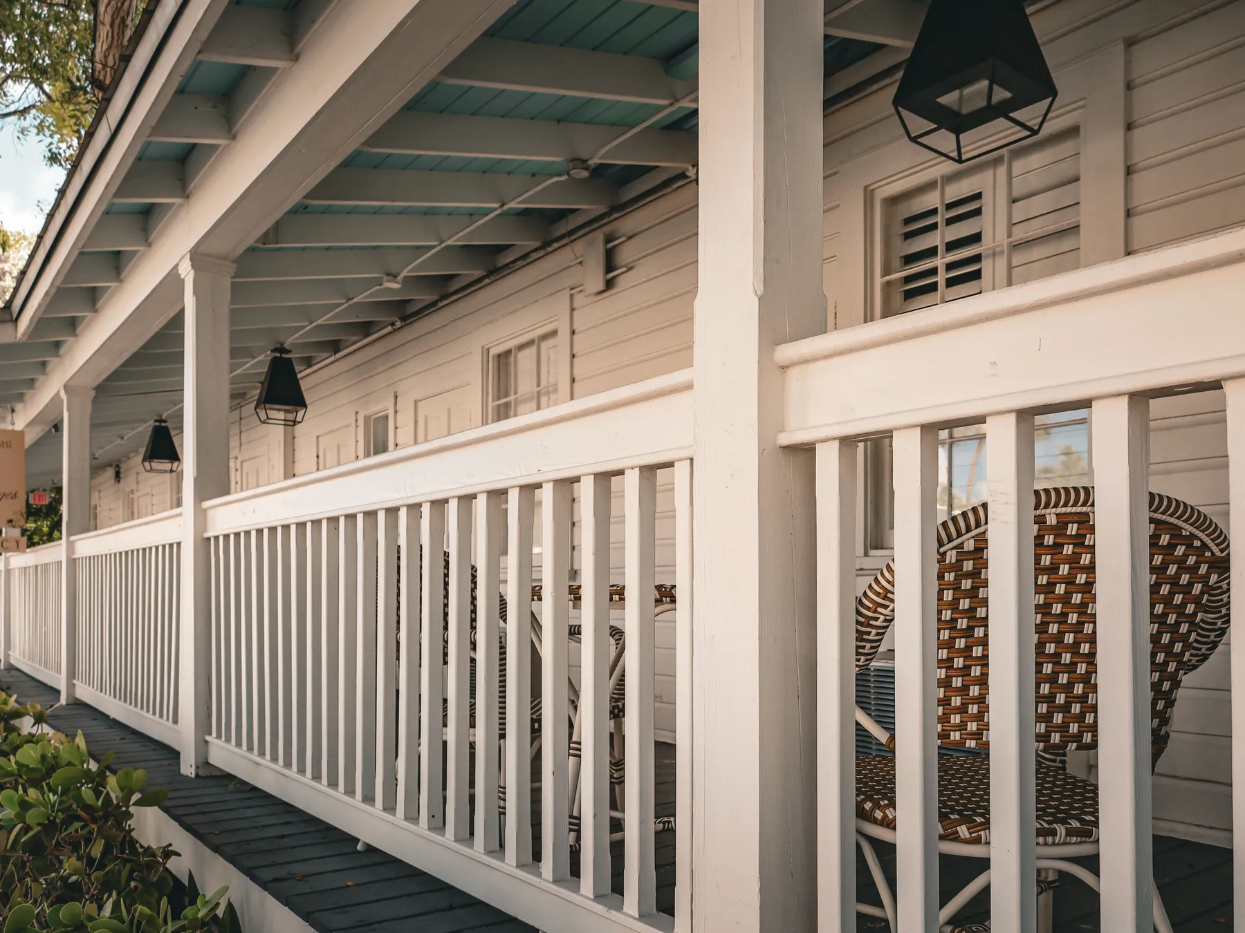 A long wooden porch with white railings, black lanterns and wicker chairs