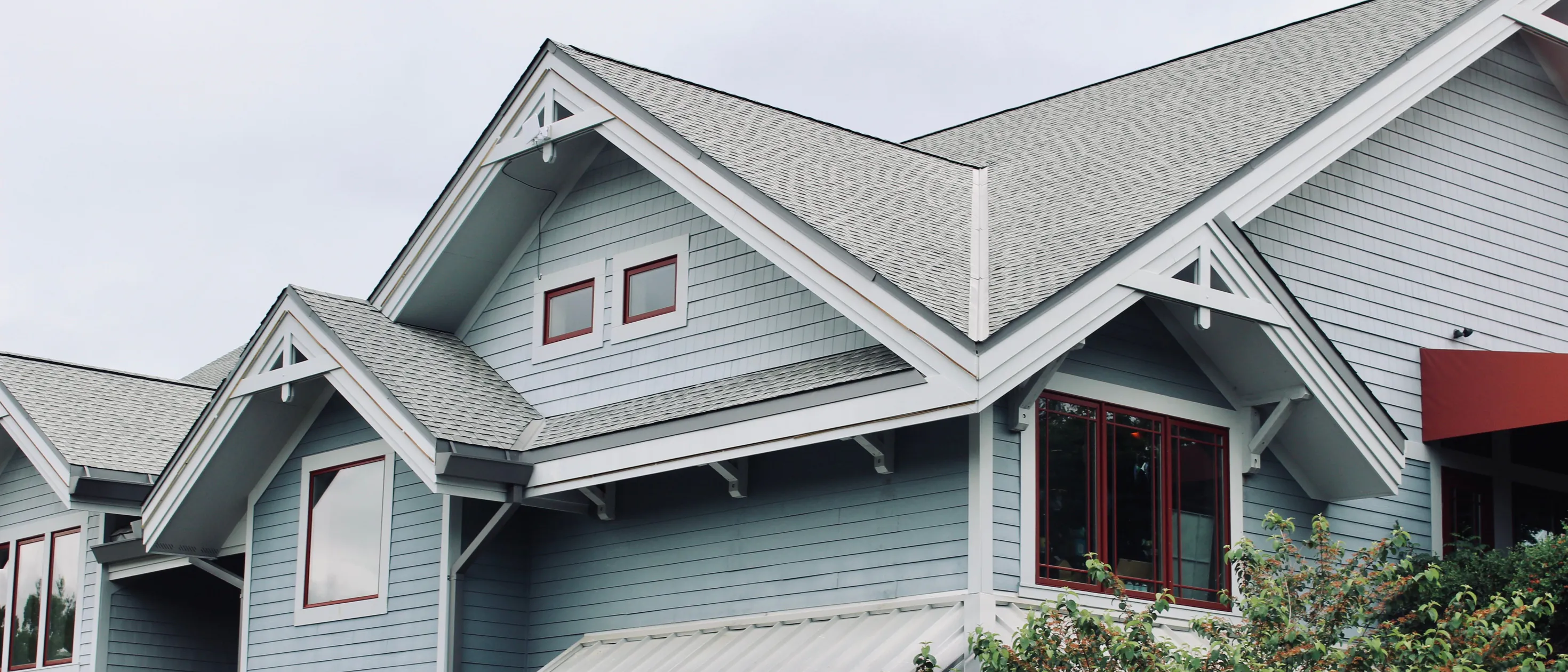 Blue-grey lap siding, white fascia and gable brackets, and red-framed windows under a grey shingle roof