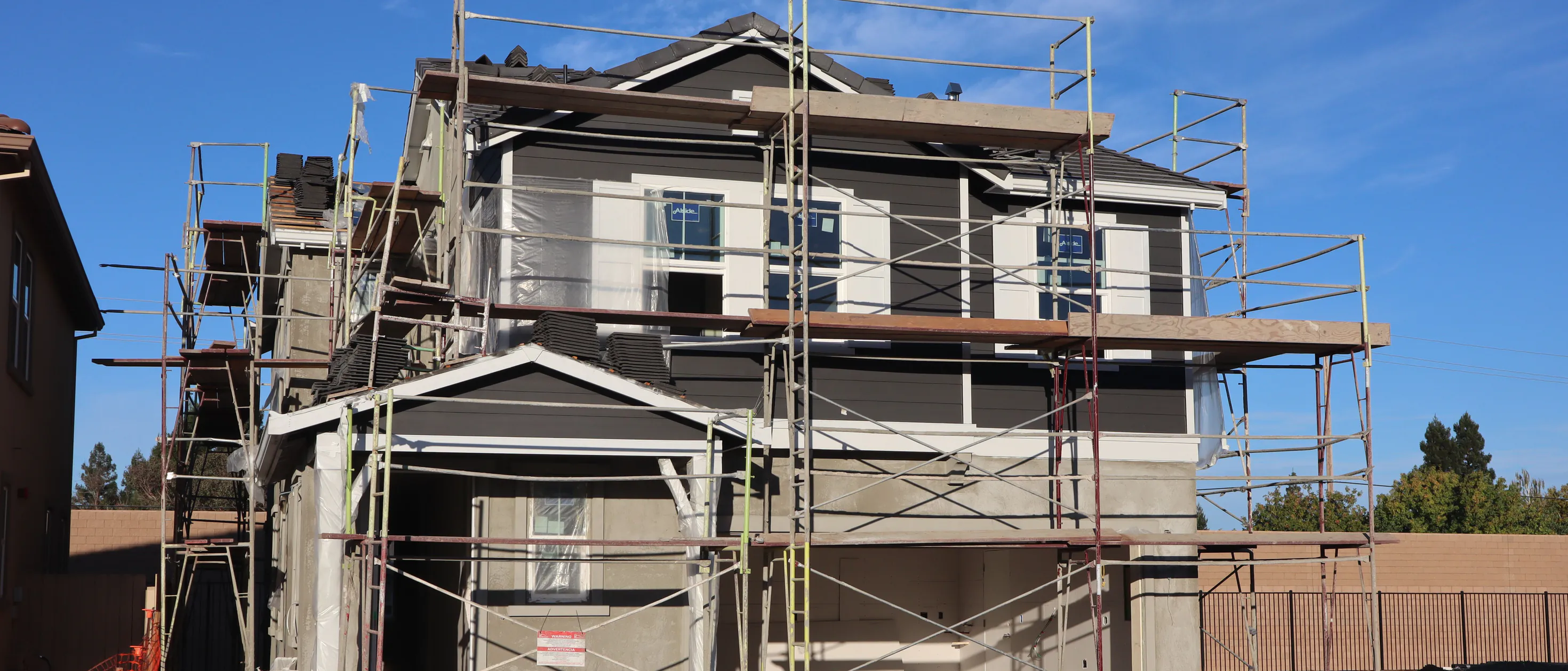 A two-storey house wrapped in scaffolding while its new cladding goes on