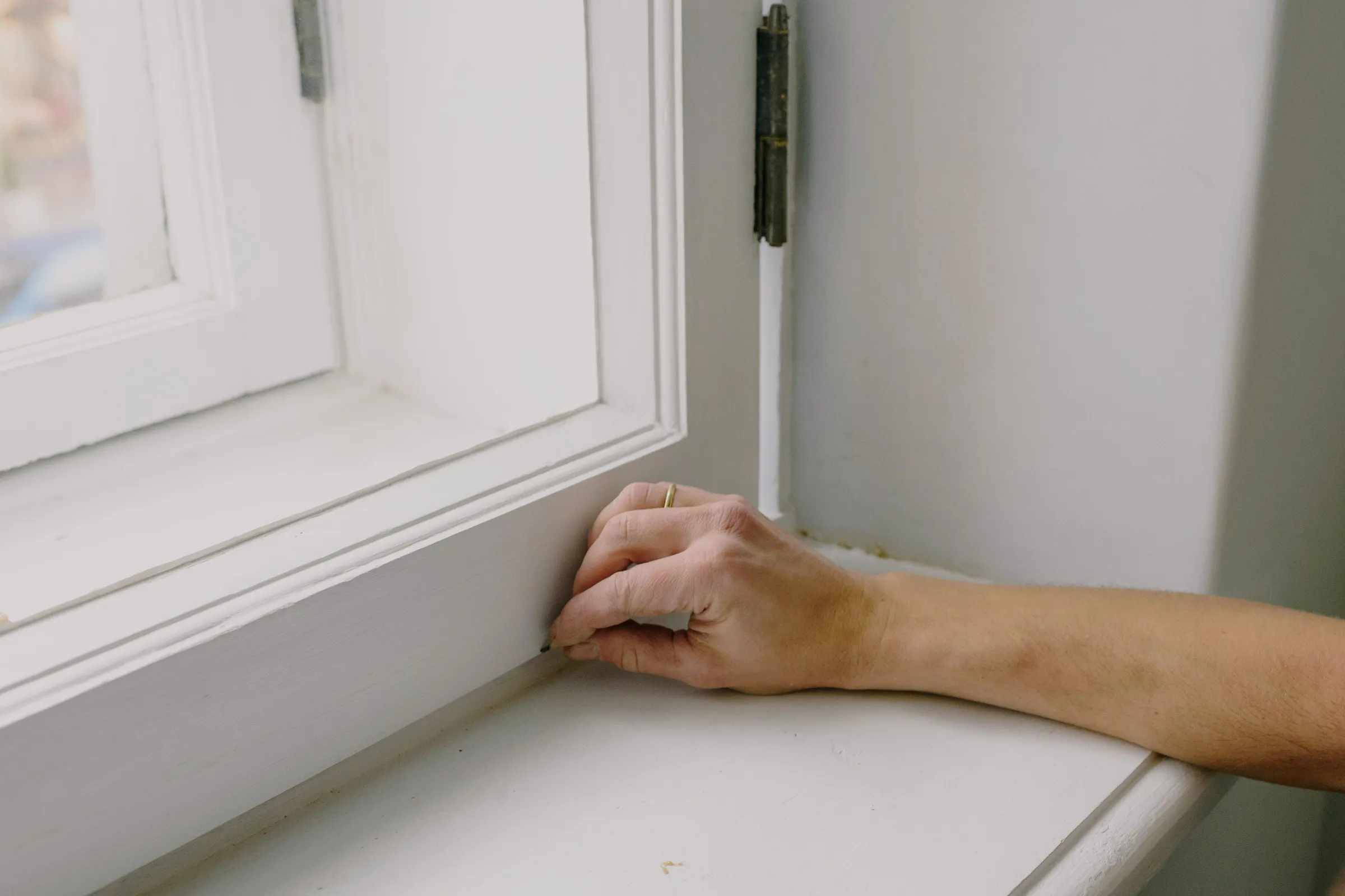 A hand resting on a white painted windowsill beside the lower casing of a sash window