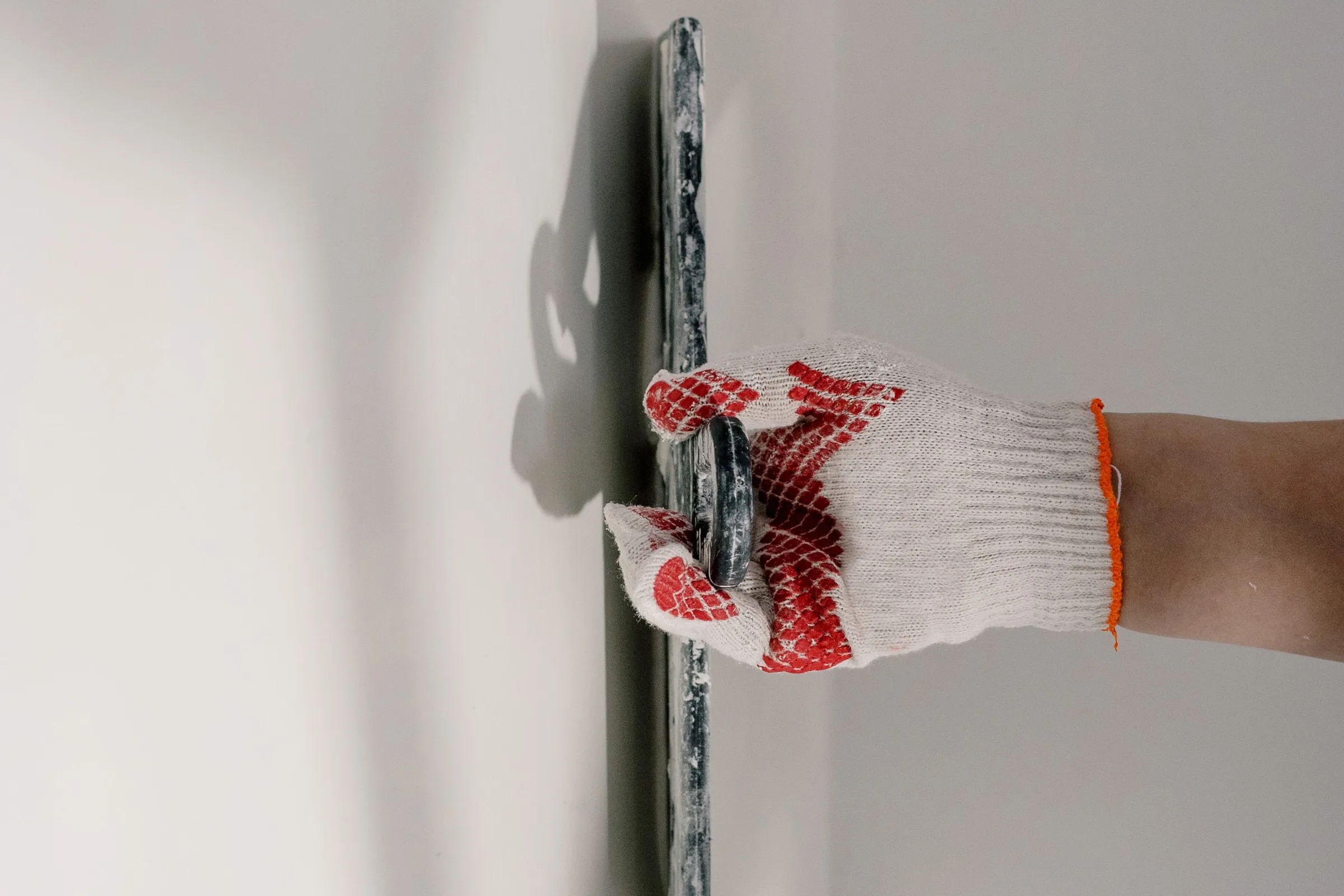 A gloved hand drawing a wide trowel down a smooth white wall