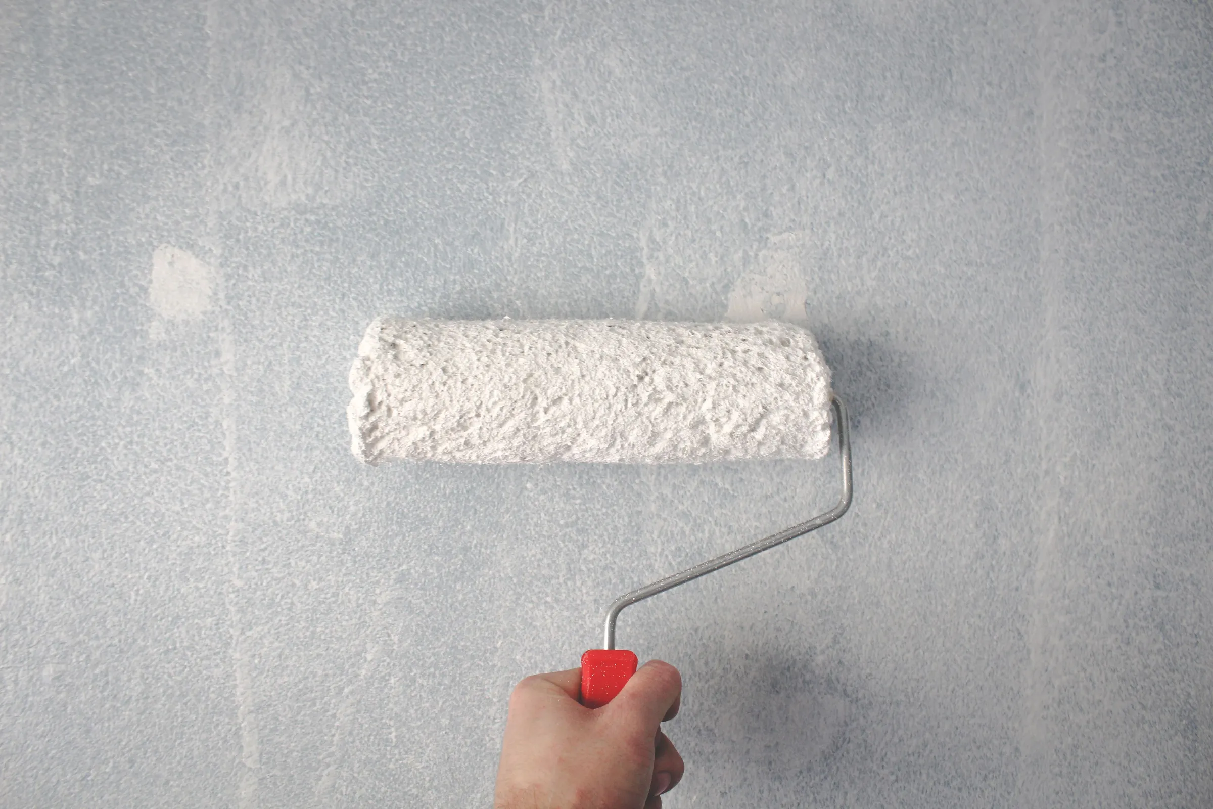 A hand rolling white paint over a grey wall