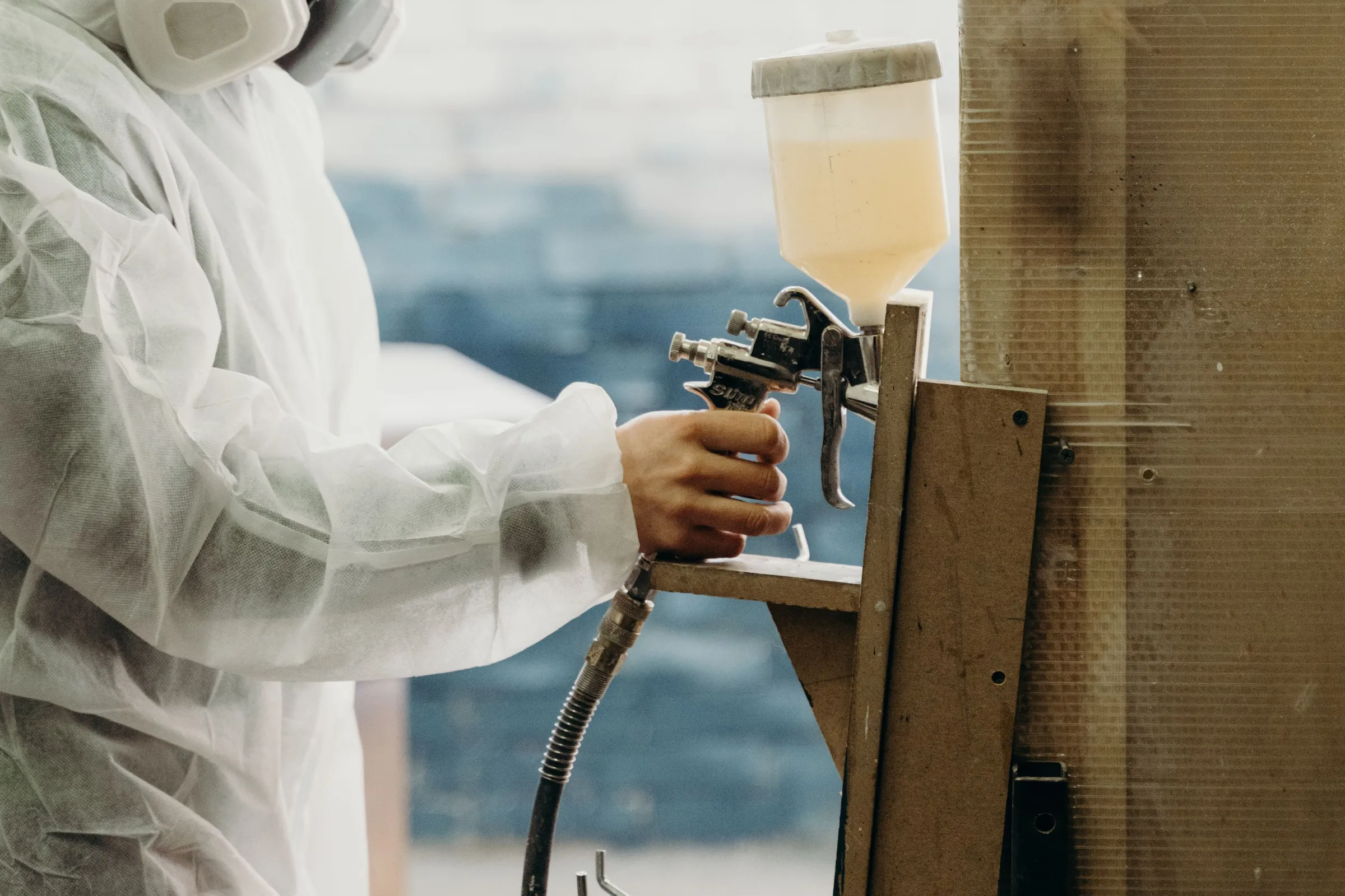 A painter in a protective suit spraying a wood panel with a gravity-feed HVLP spray gun
