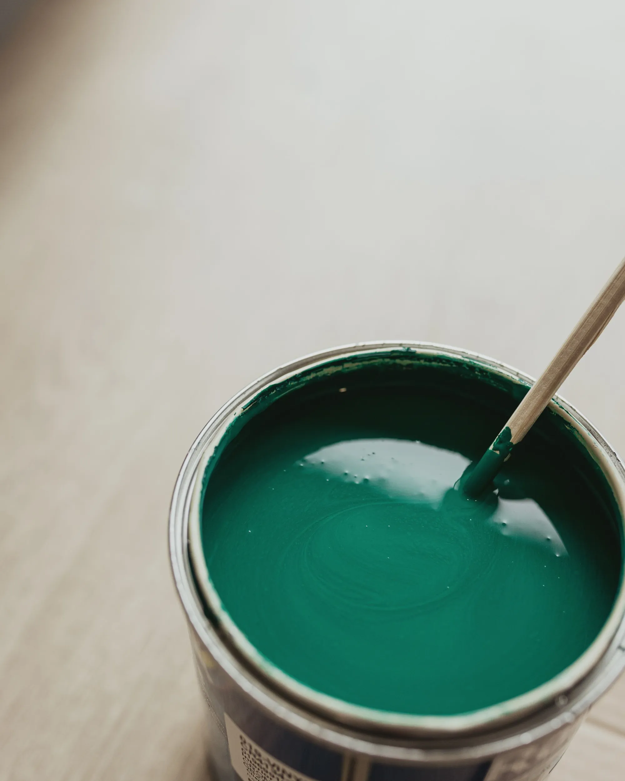 A can of deep green paint being stirred with a wooden stick