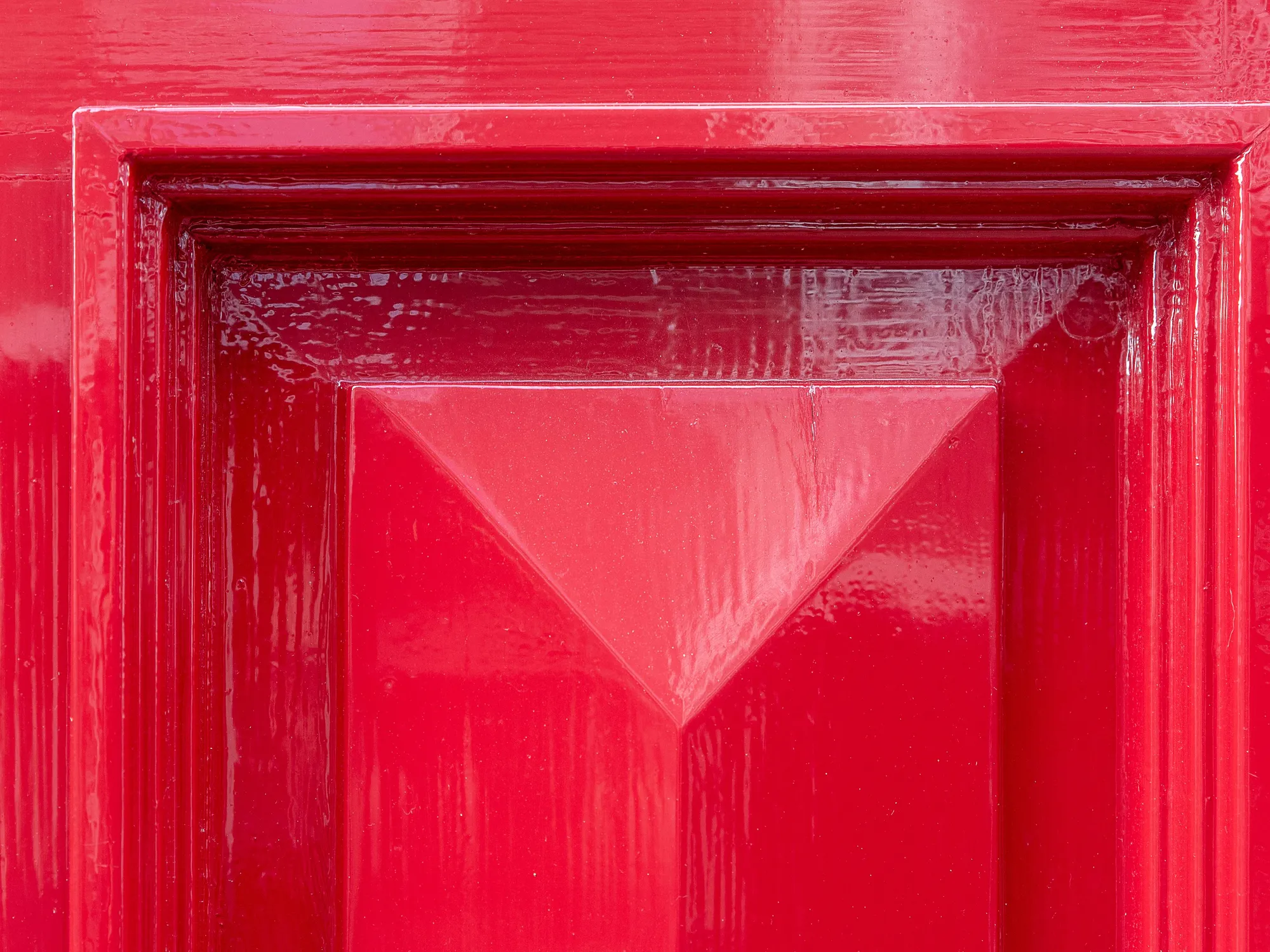 A red high-gloss door panel close up, its raised field and mouldings throwing sharp reflections