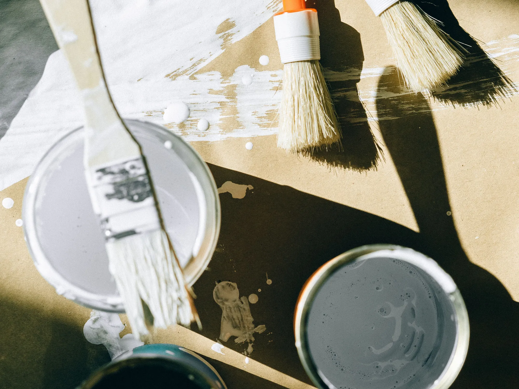 Paintbrushes and open cans of white and grey paint in low sunlight