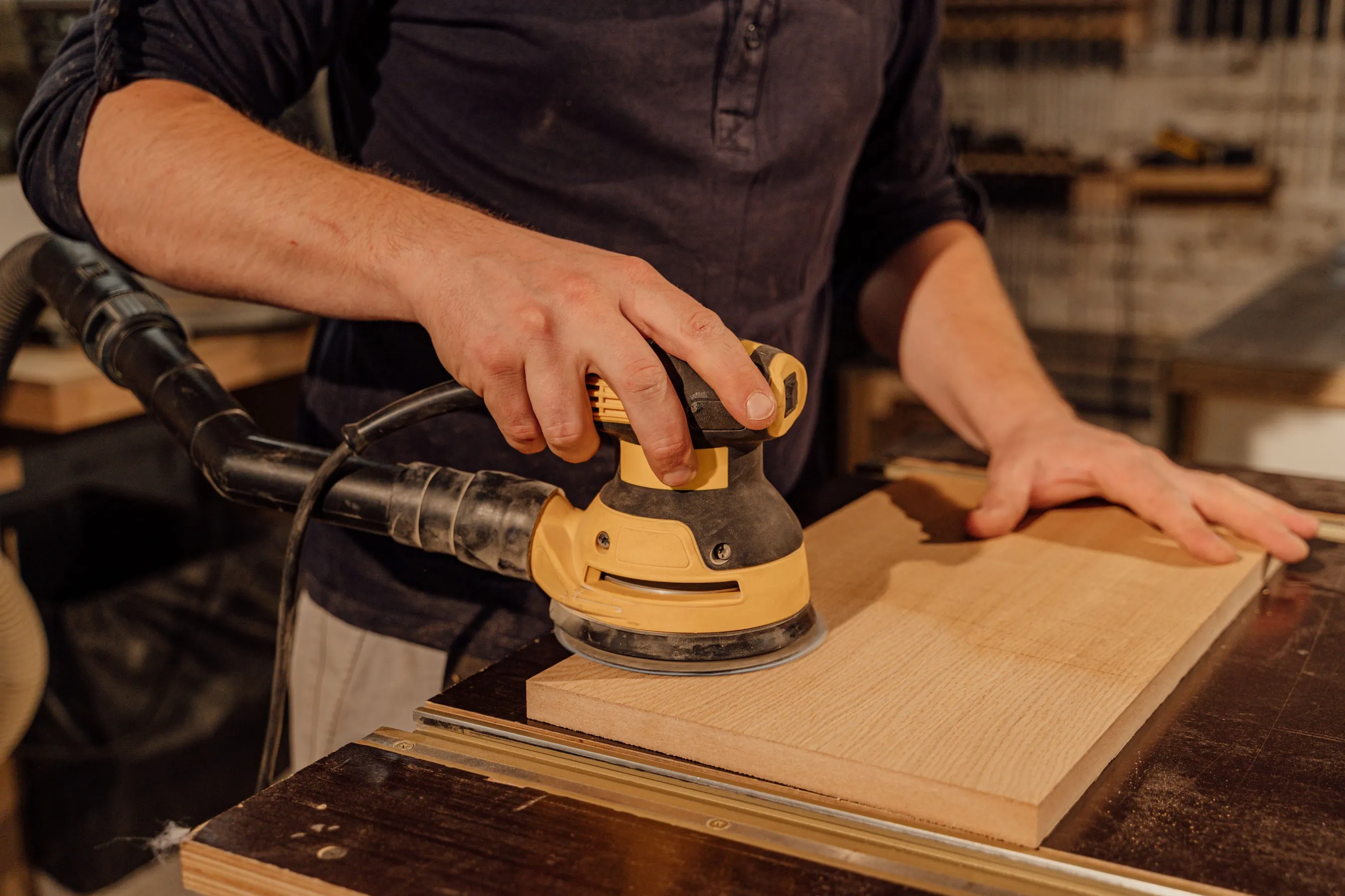 Two hands guiding an orbital sander across a pale wood board