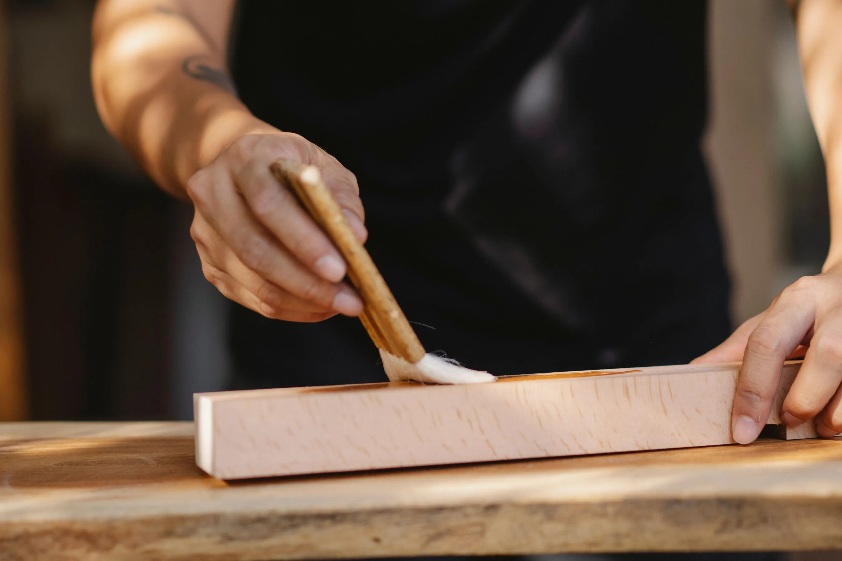 A hand brushing a first coat onto a length of bare wood