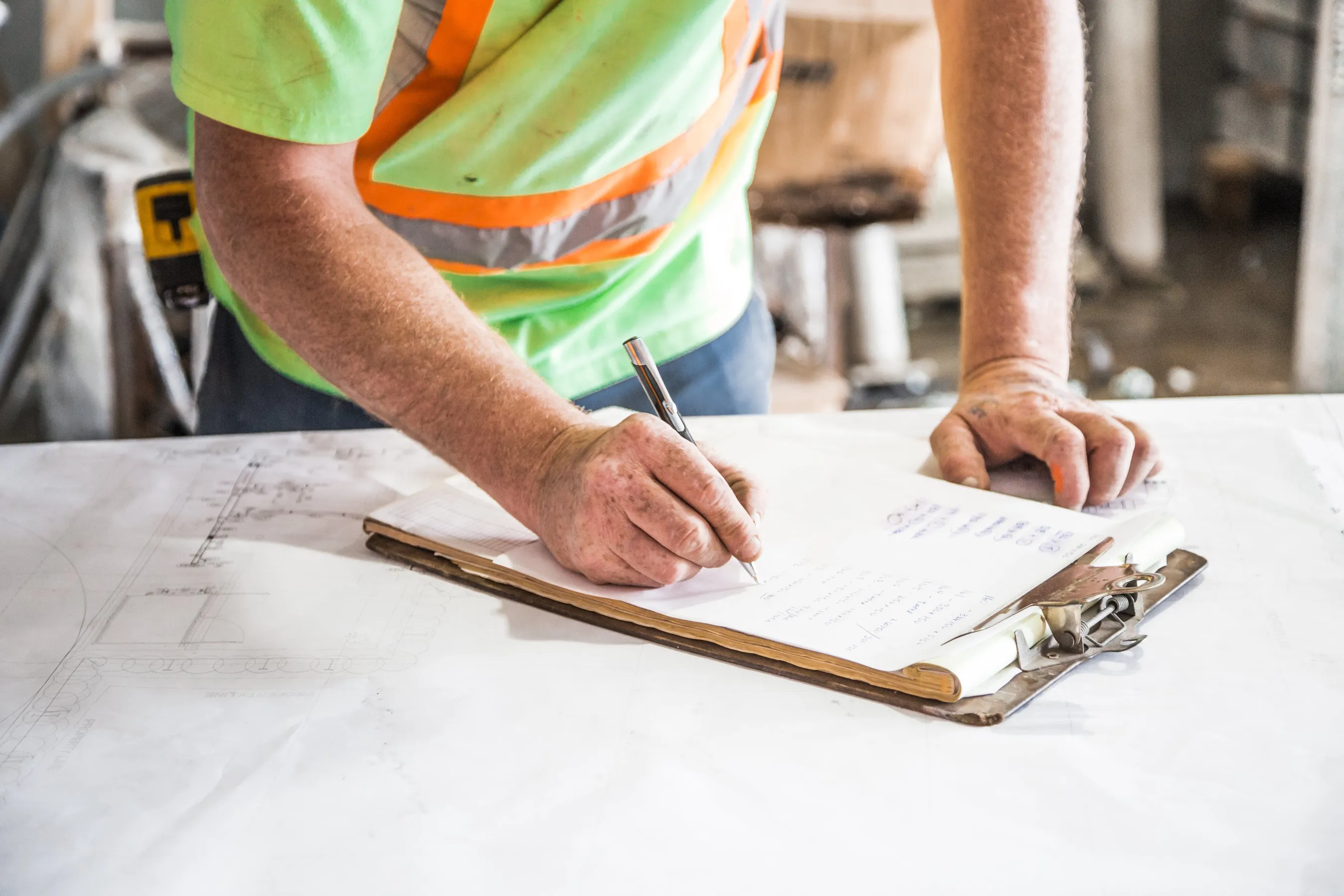A hand filling in a form on a clipboard laid over a set of drawings