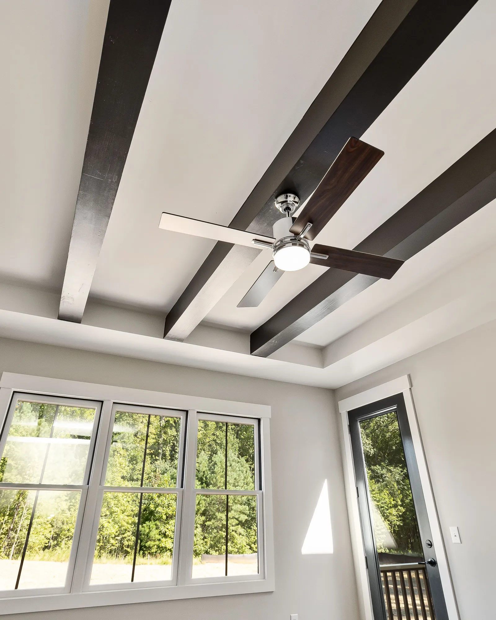 A bright white room with dark exposed ceiling beams, a ceiling fan and tall windows