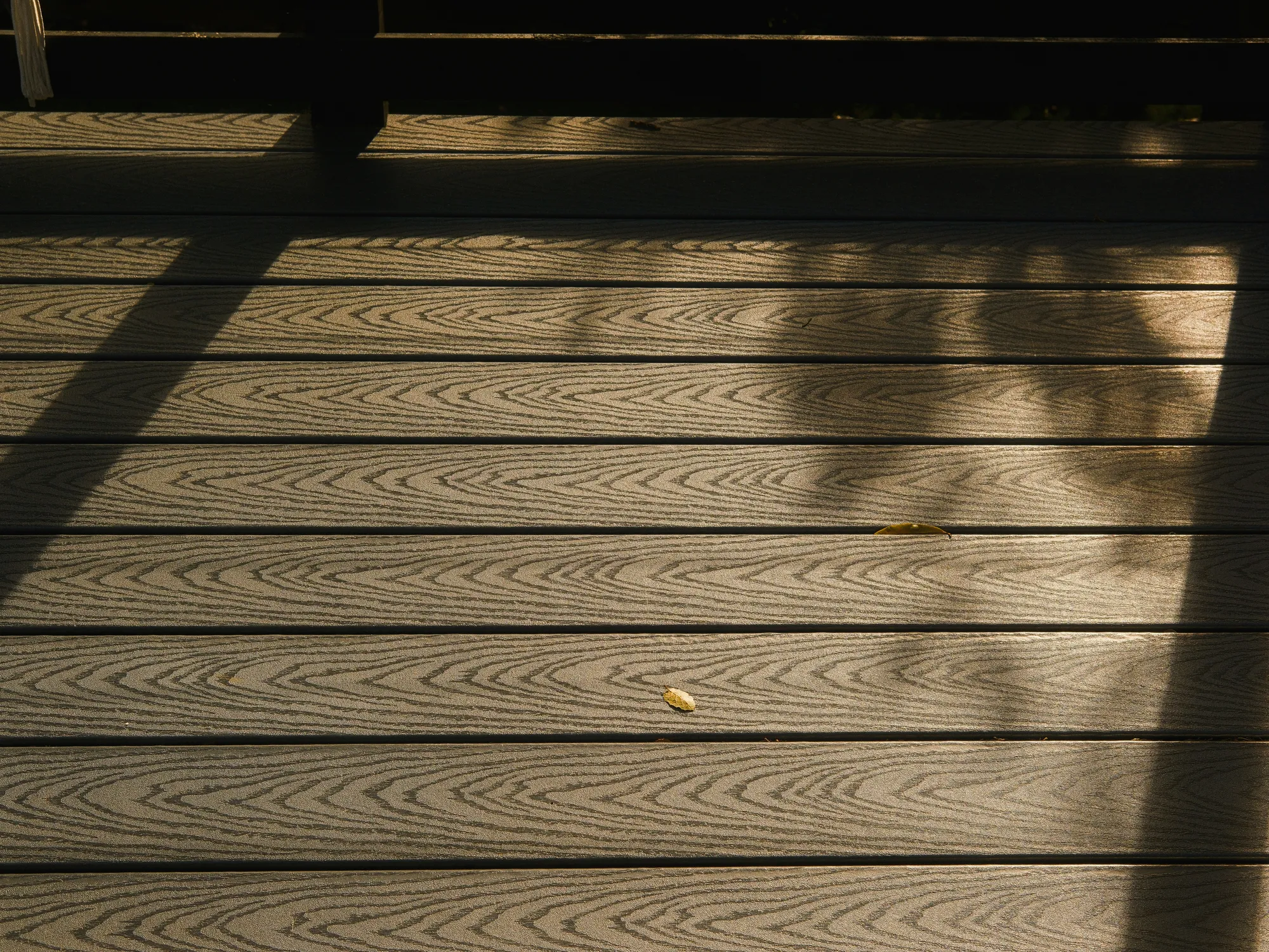 Gray composite deck boards with a printed wood grain, crossed by long shadows