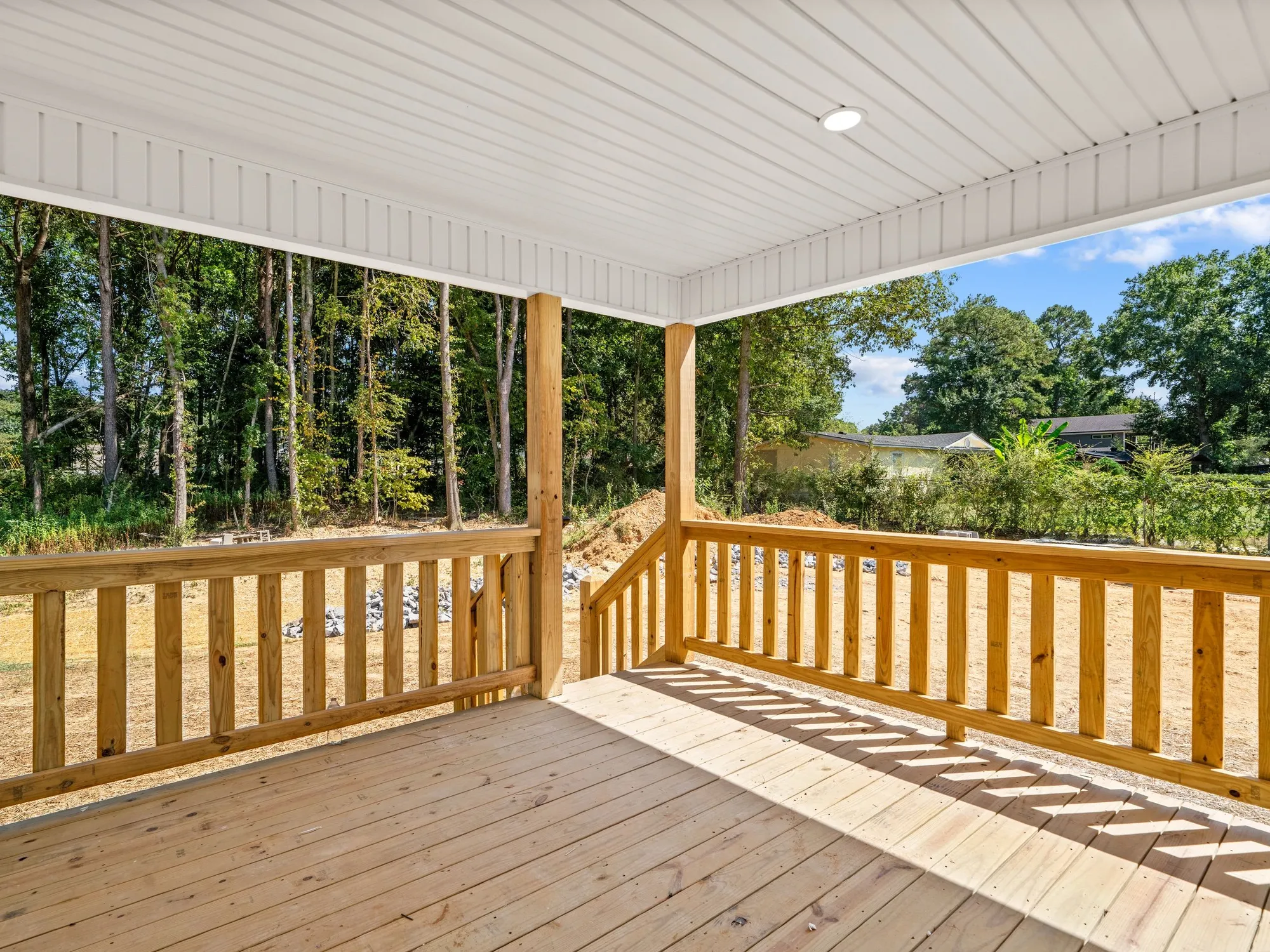Pale wood deck boards and a wood railing on a covered porch looking out to trees