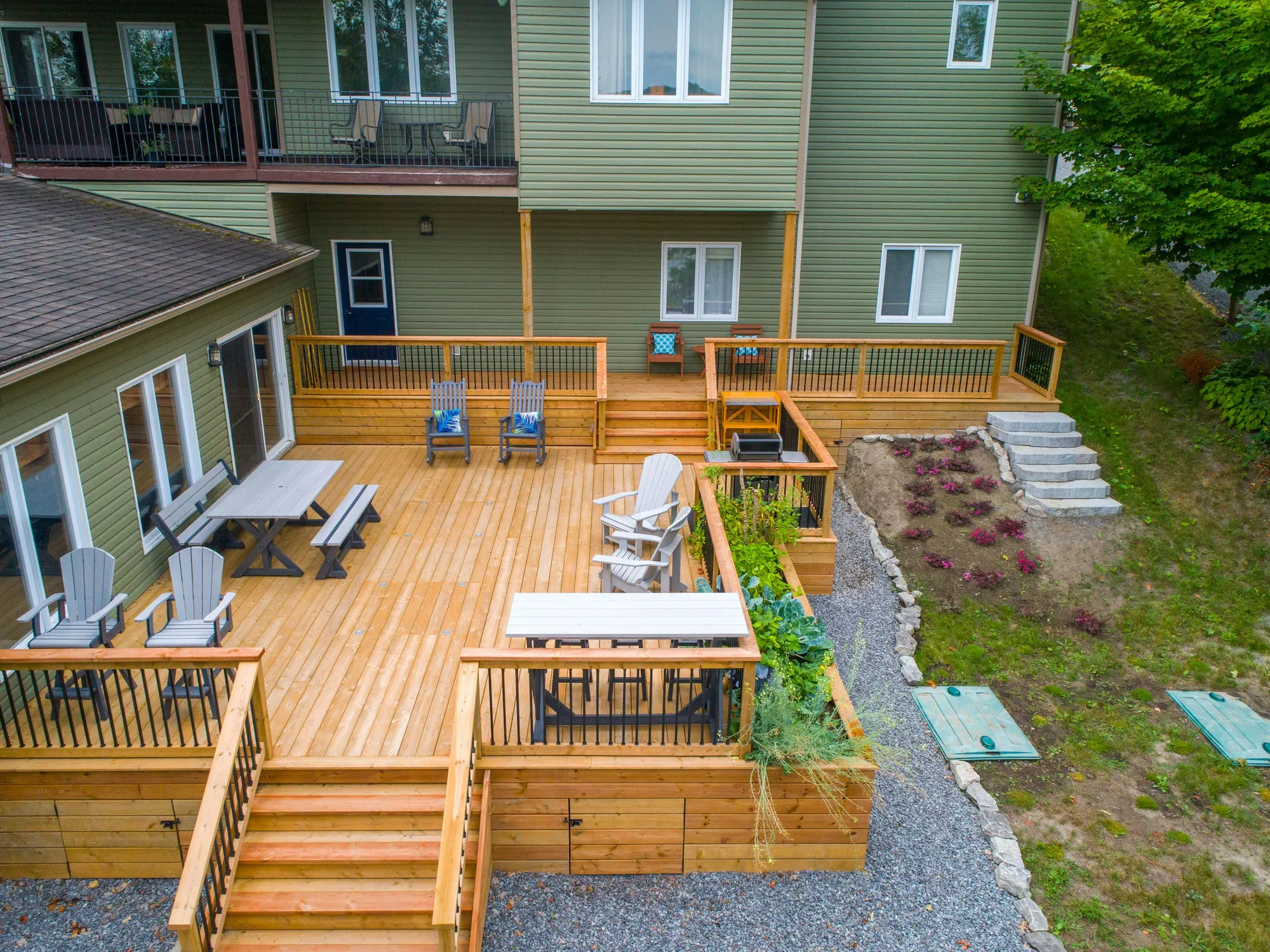 A new two-level cedar deck with railings, stairs and outdoor furniture behind a green house
