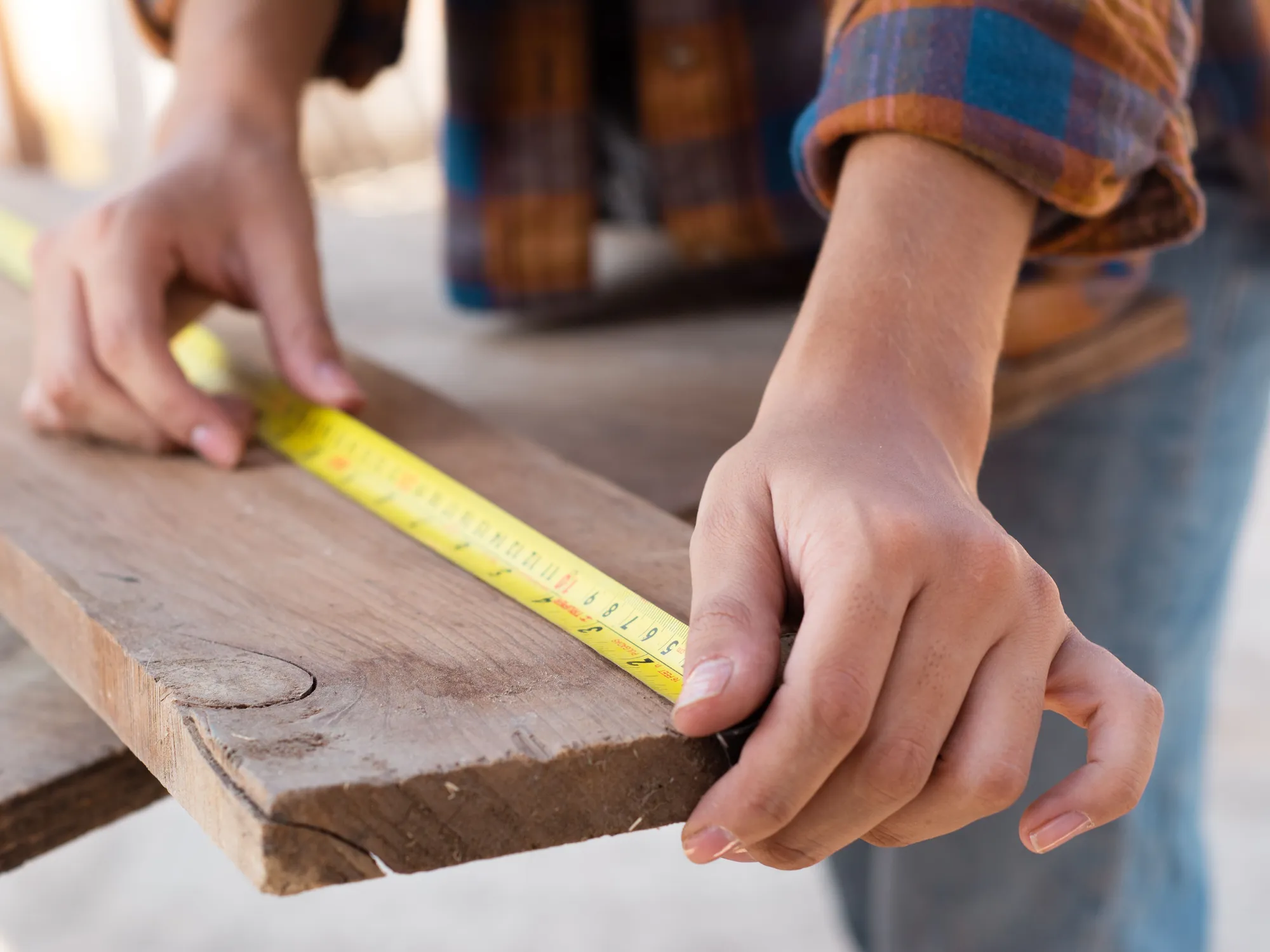 Two hands holding a tape measure along the edge of a weathered wood board