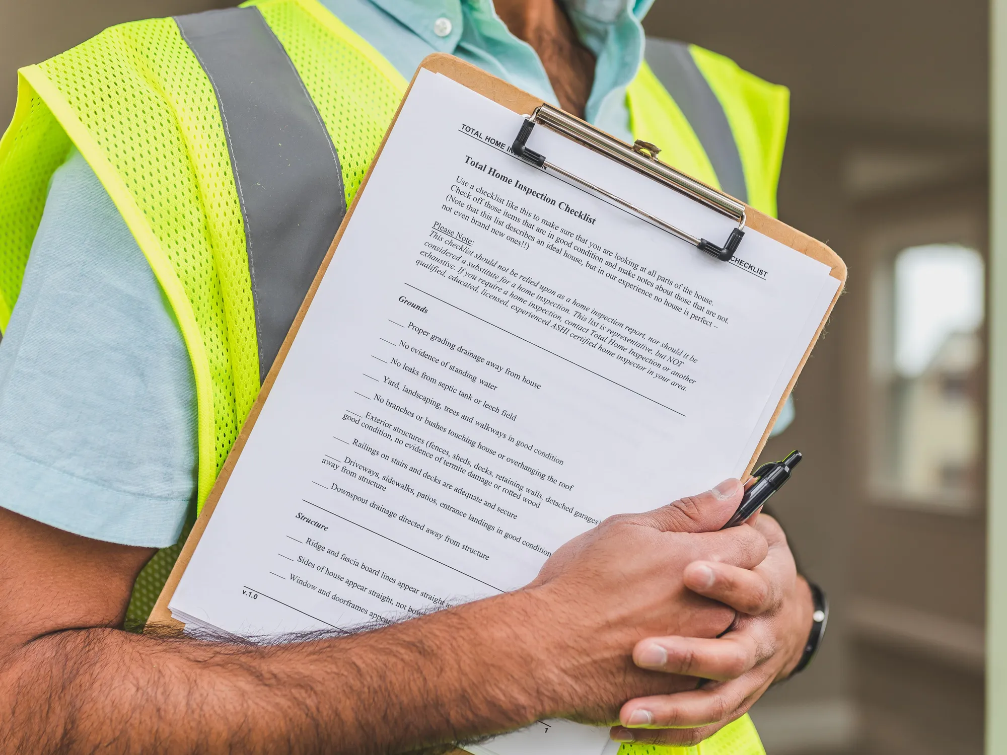 A printed checklist on a clipboard held against a yellow safety vest, pen in hand
