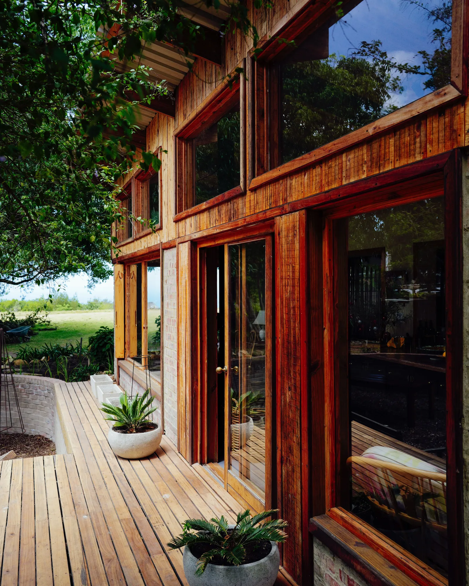 A wood deck running along a timber-clad house with tall windows and potted plants