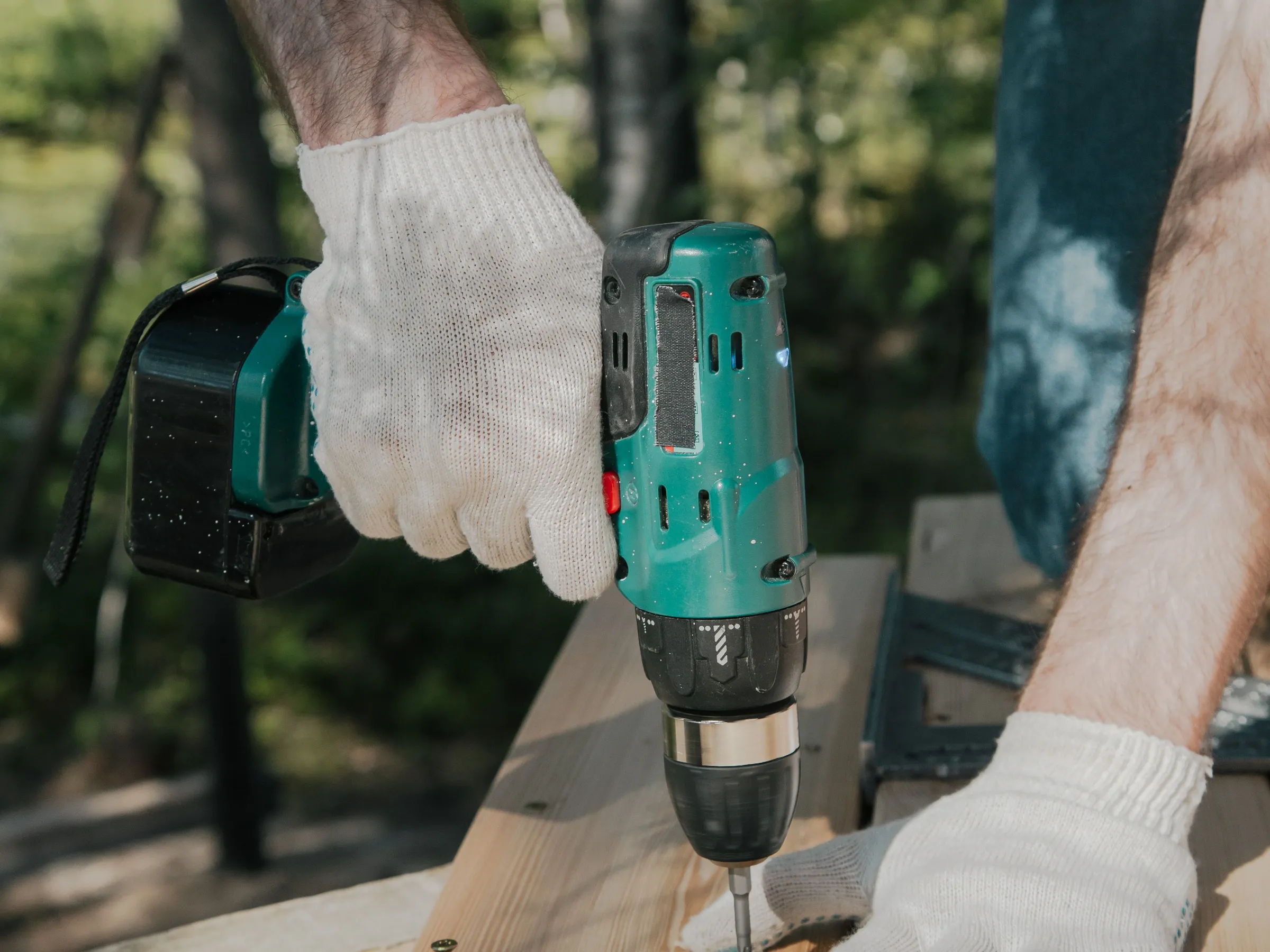 Gloved hands driving a screw into new deck boards with a cordless drill