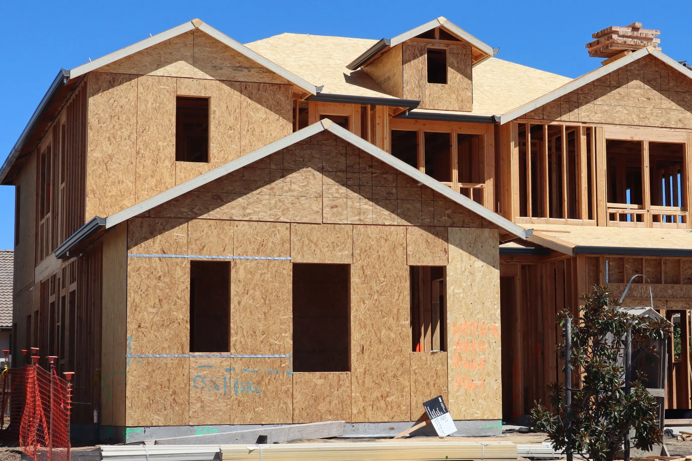 A two-storey house frame clad in bare OSB sheathing, its window openings cut and no siding on yet