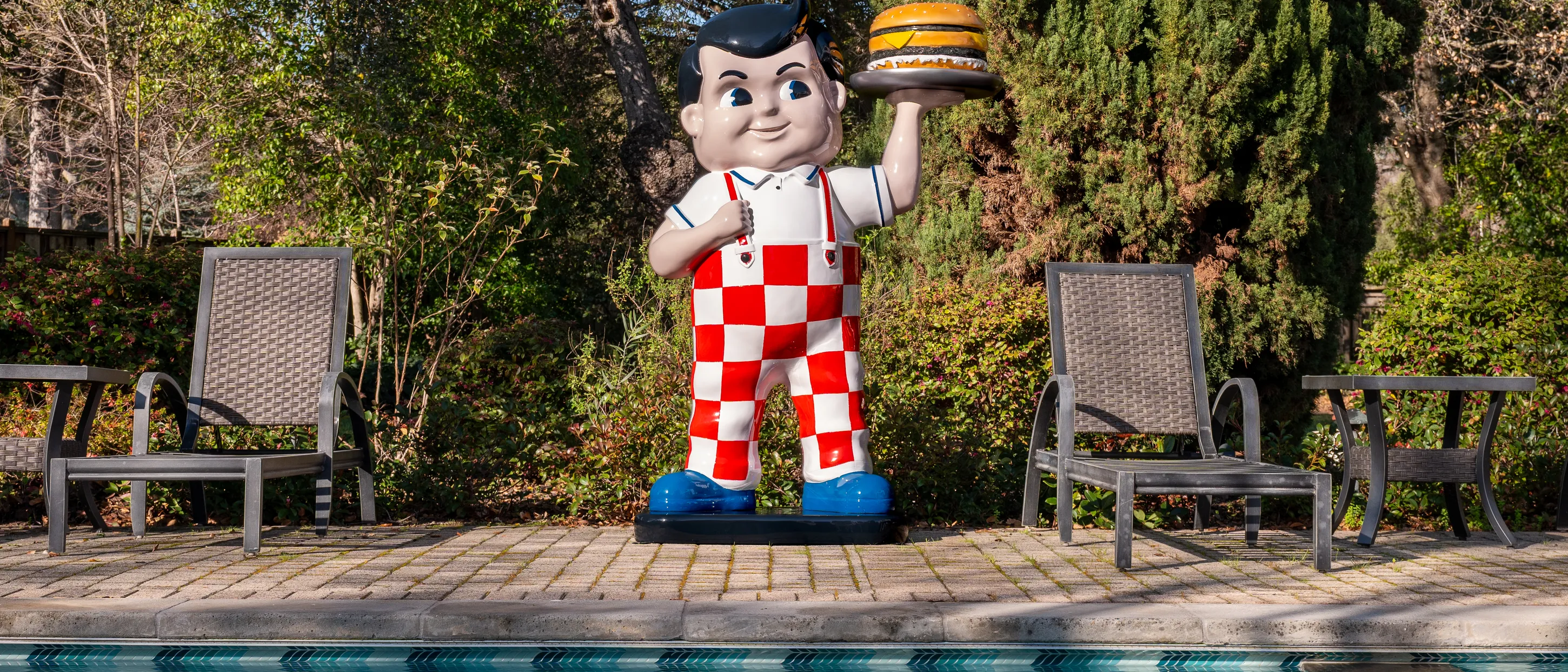 The restored Big Boy statue standing on a poolside terrace between two garden chairs