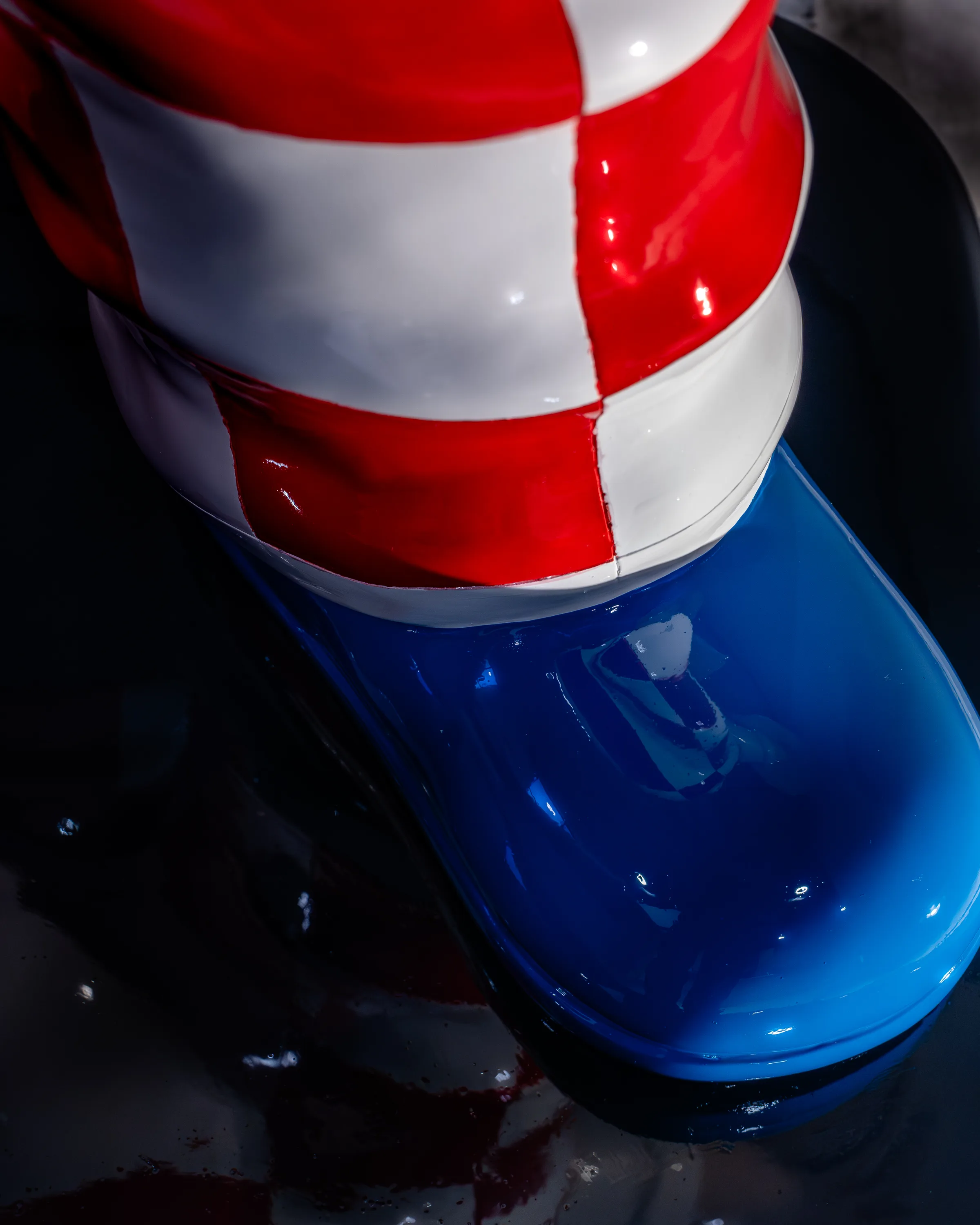A close view of the statue's glossy blue shoe and checked trouser cuff, the enamel reflecting the room