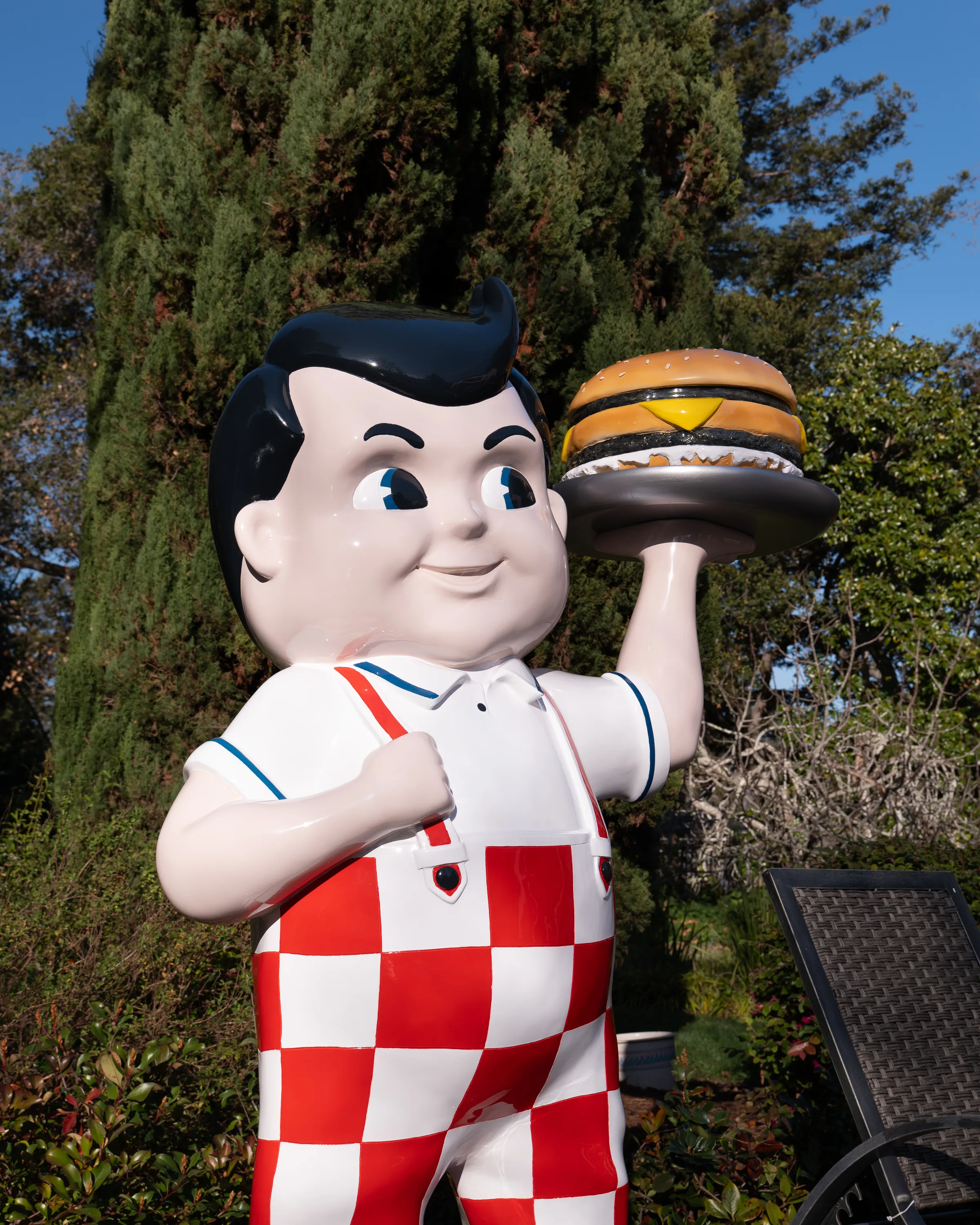 The restored Big Boy statue in mirror-gloss red, white and blue, holding its burger tray up in a sunlit garden