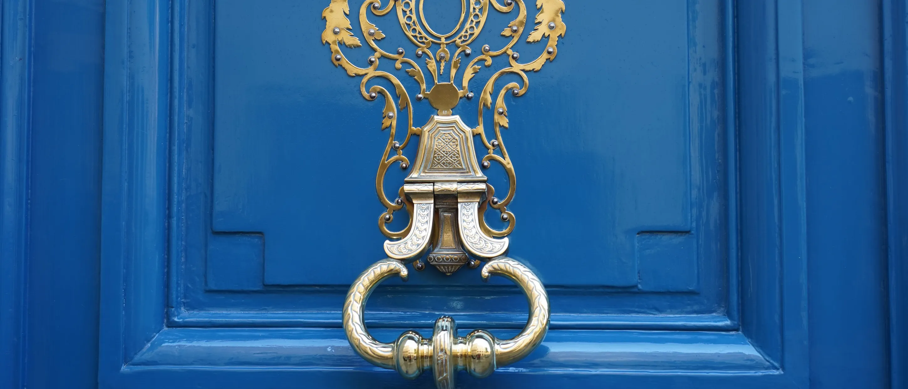 A rich blue high-gloss panelled door with an ornate polished brass knocker