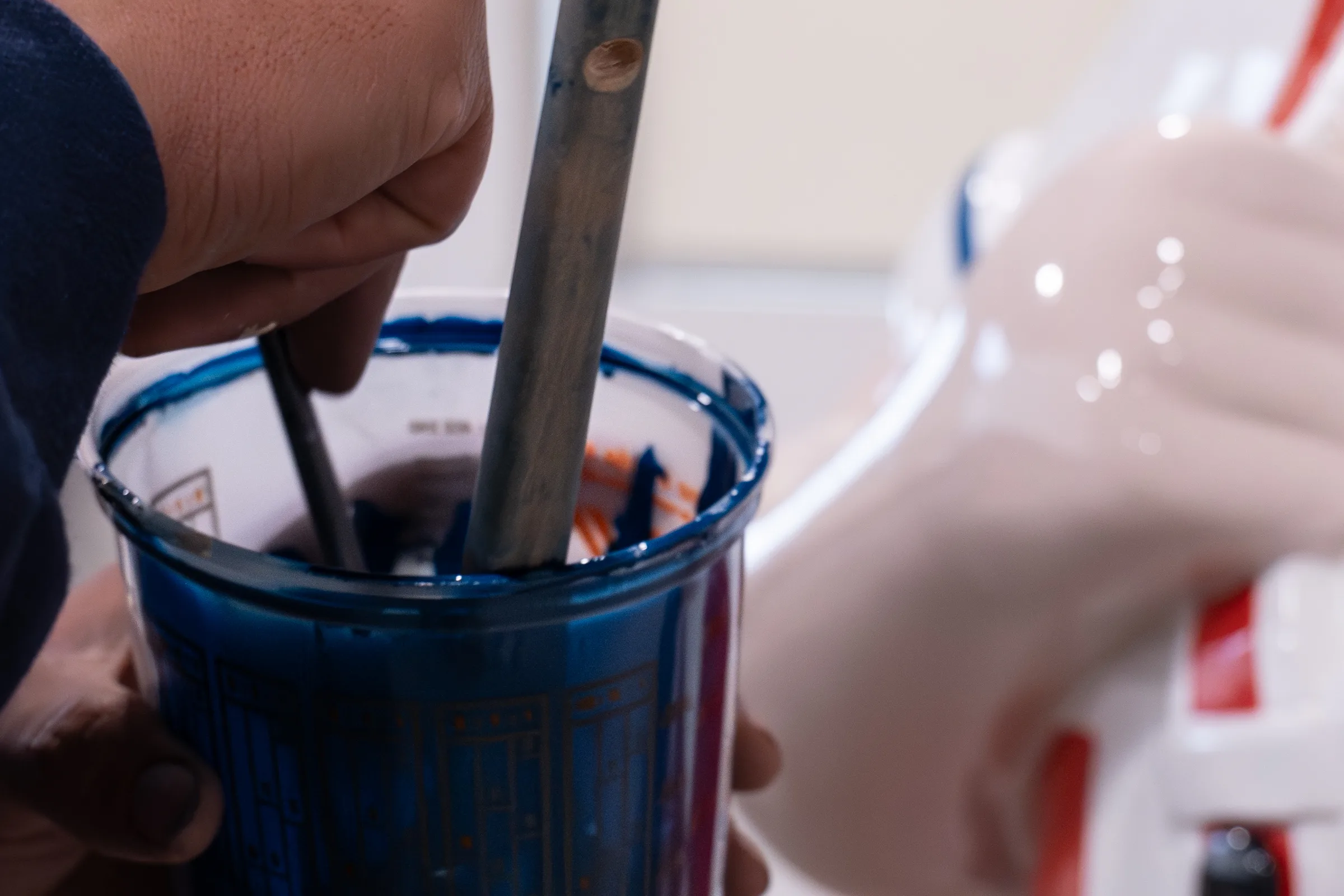 A painter's hand holding a cup of navy enamel with a brush in it, beside the statue