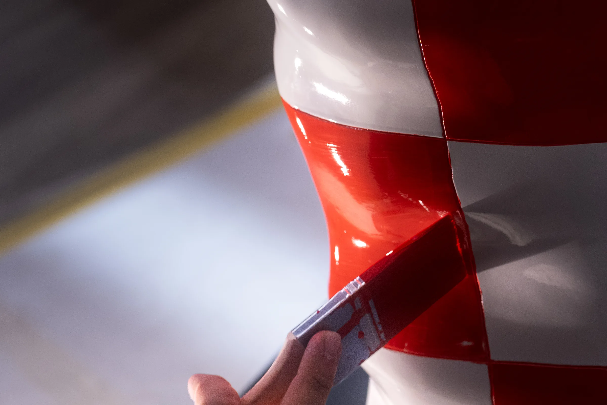 A hand laying red enamel along the checked pattern of the glossy white statue with a fine brush