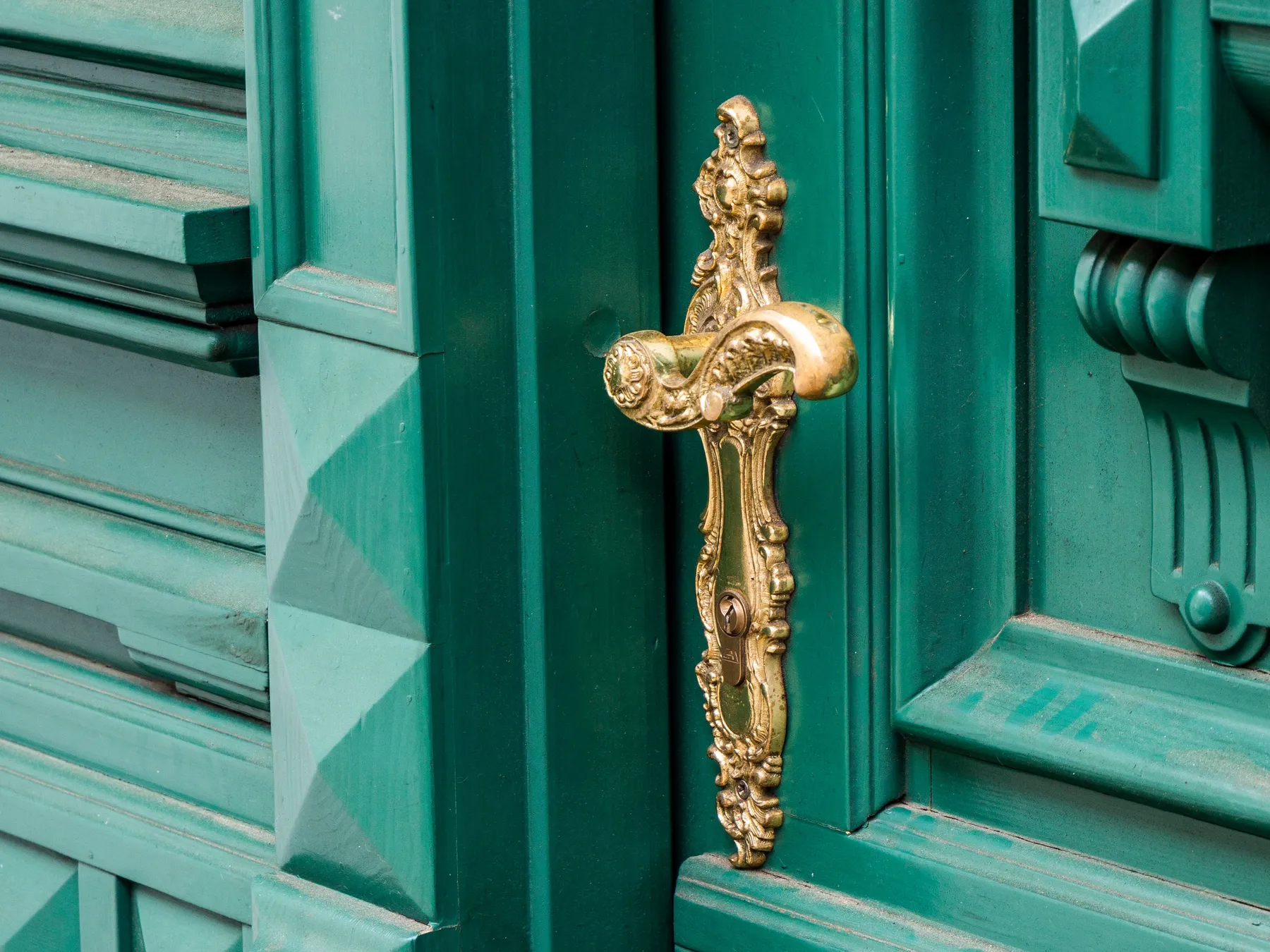 An ornate brass handle on a glossy teal panelled door