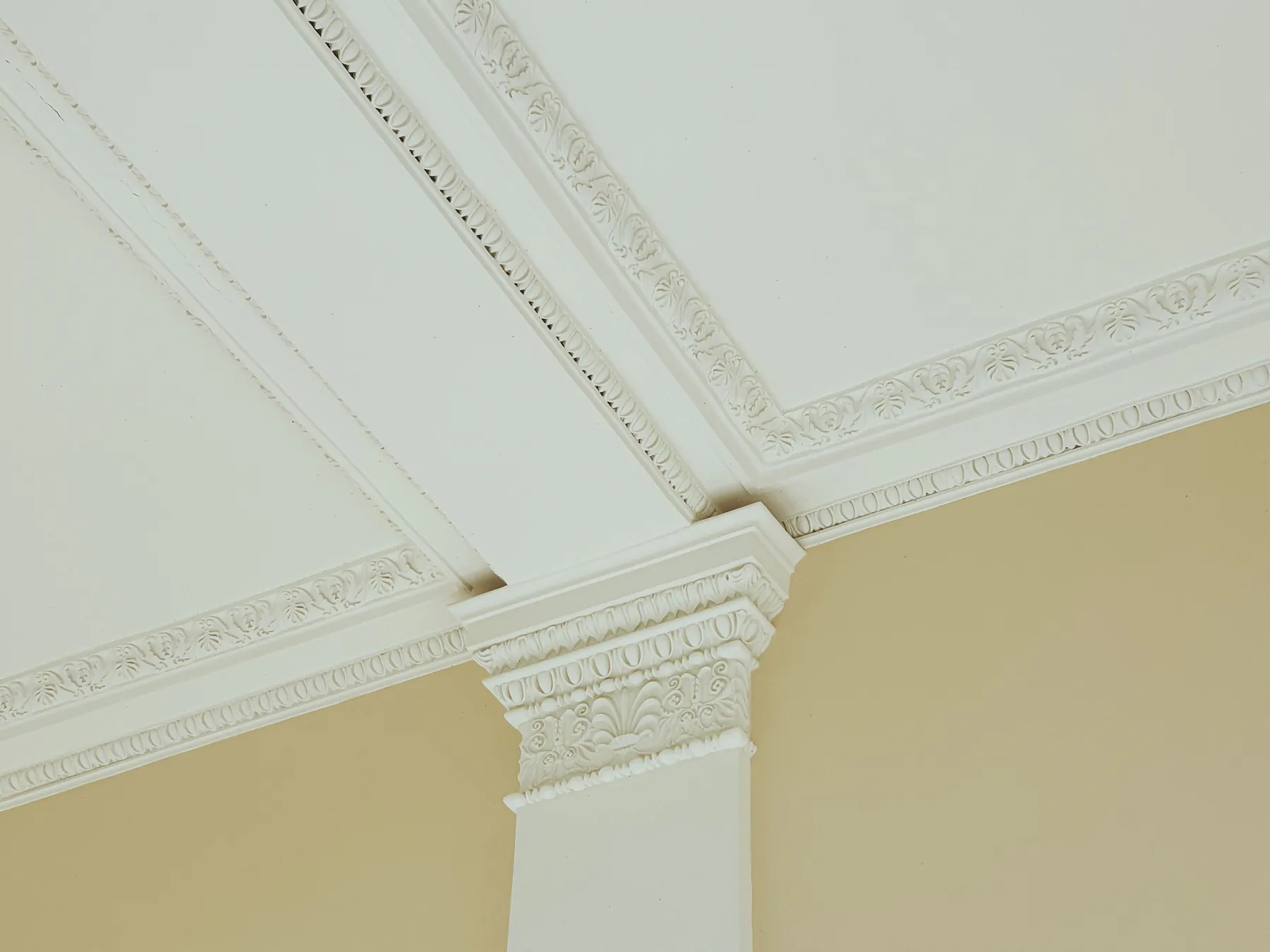 A white ornamental crown moulding and pilaster capital against a soft yellow wall