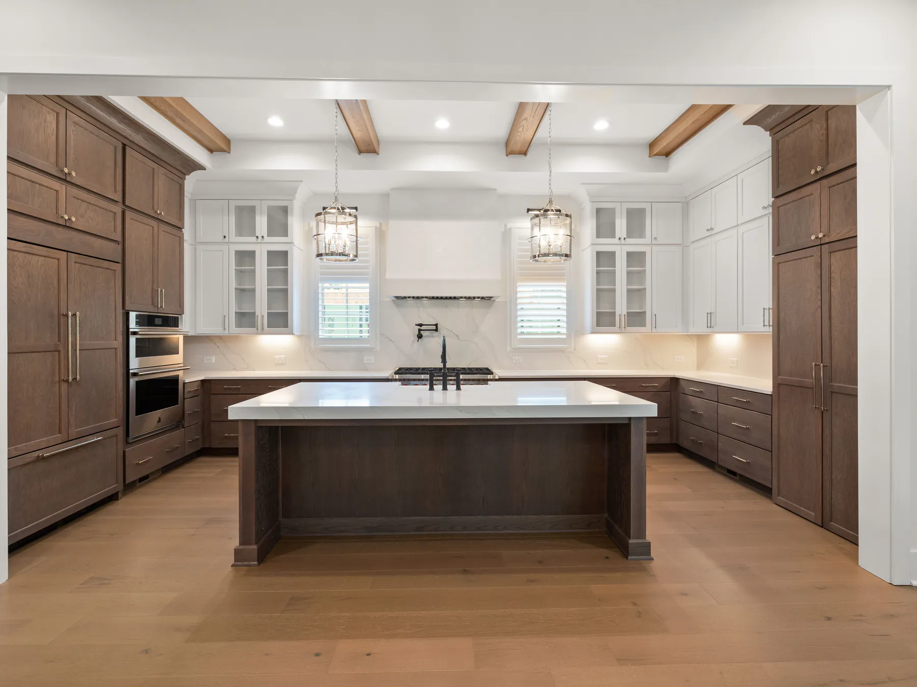 A kitchen with white upper cabinets, dark stained lower cabinets, a beamed ceiling and a central island