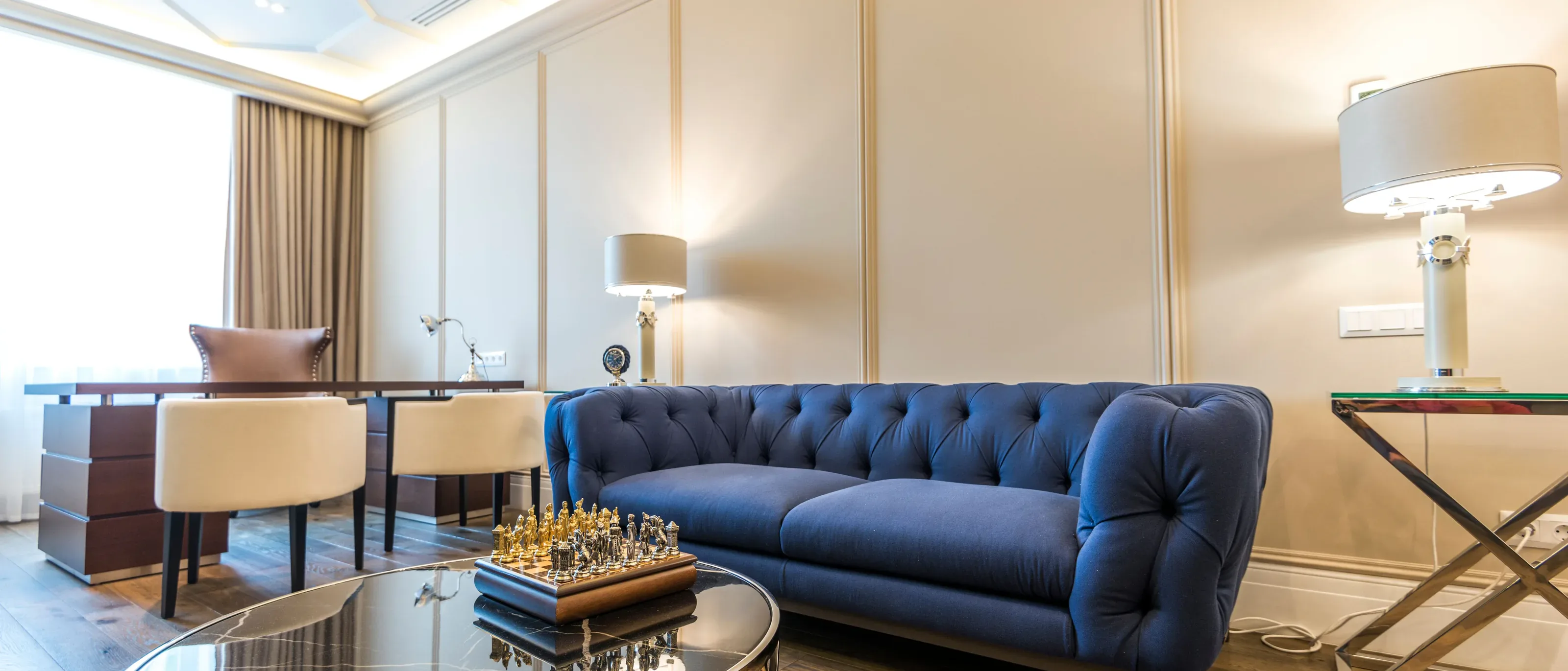 A living room with cream painted wall panels and moulding, a navy tufted sofa and warm lamps