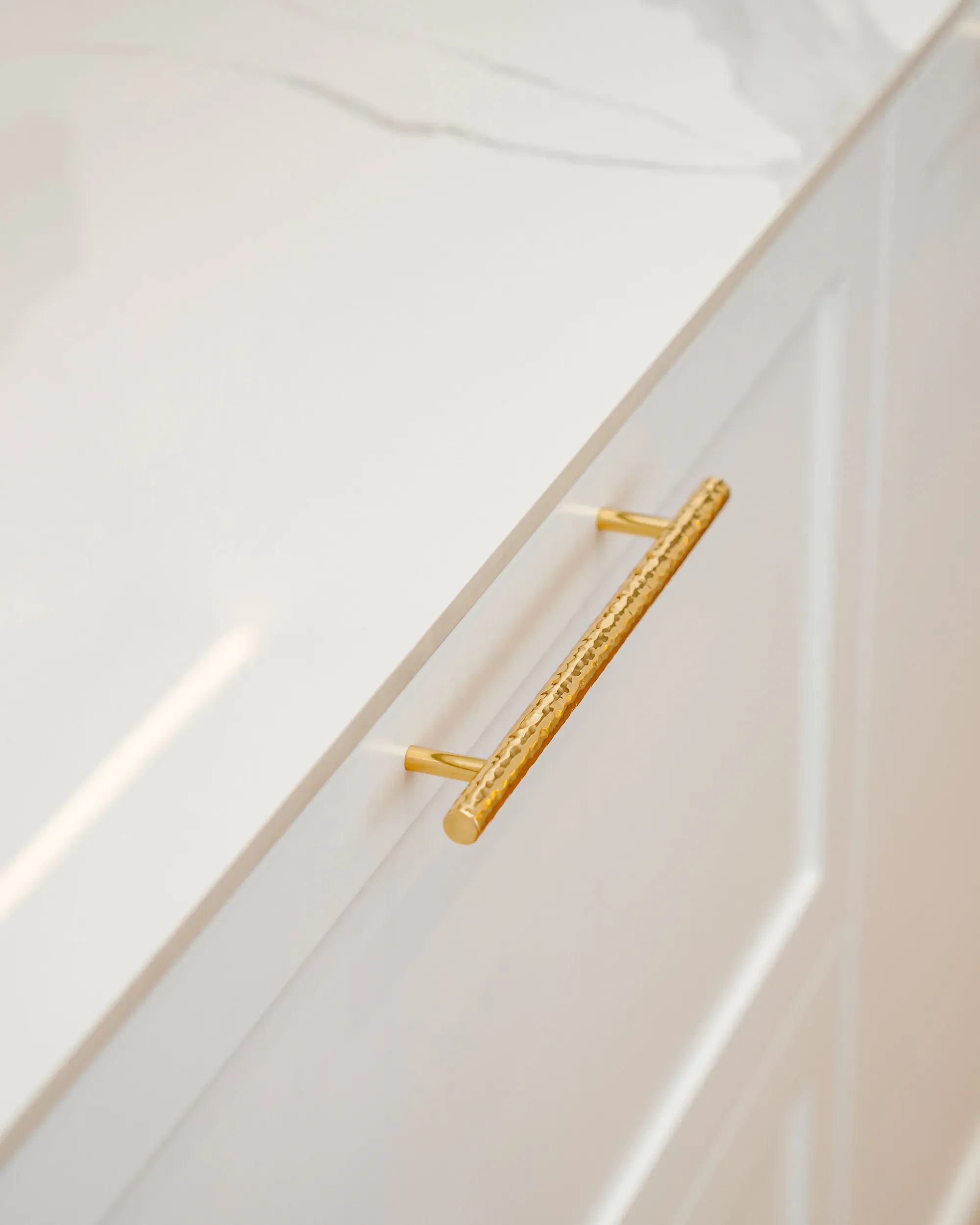 A smooth white painted cabinet front with a brass pull under a marble top