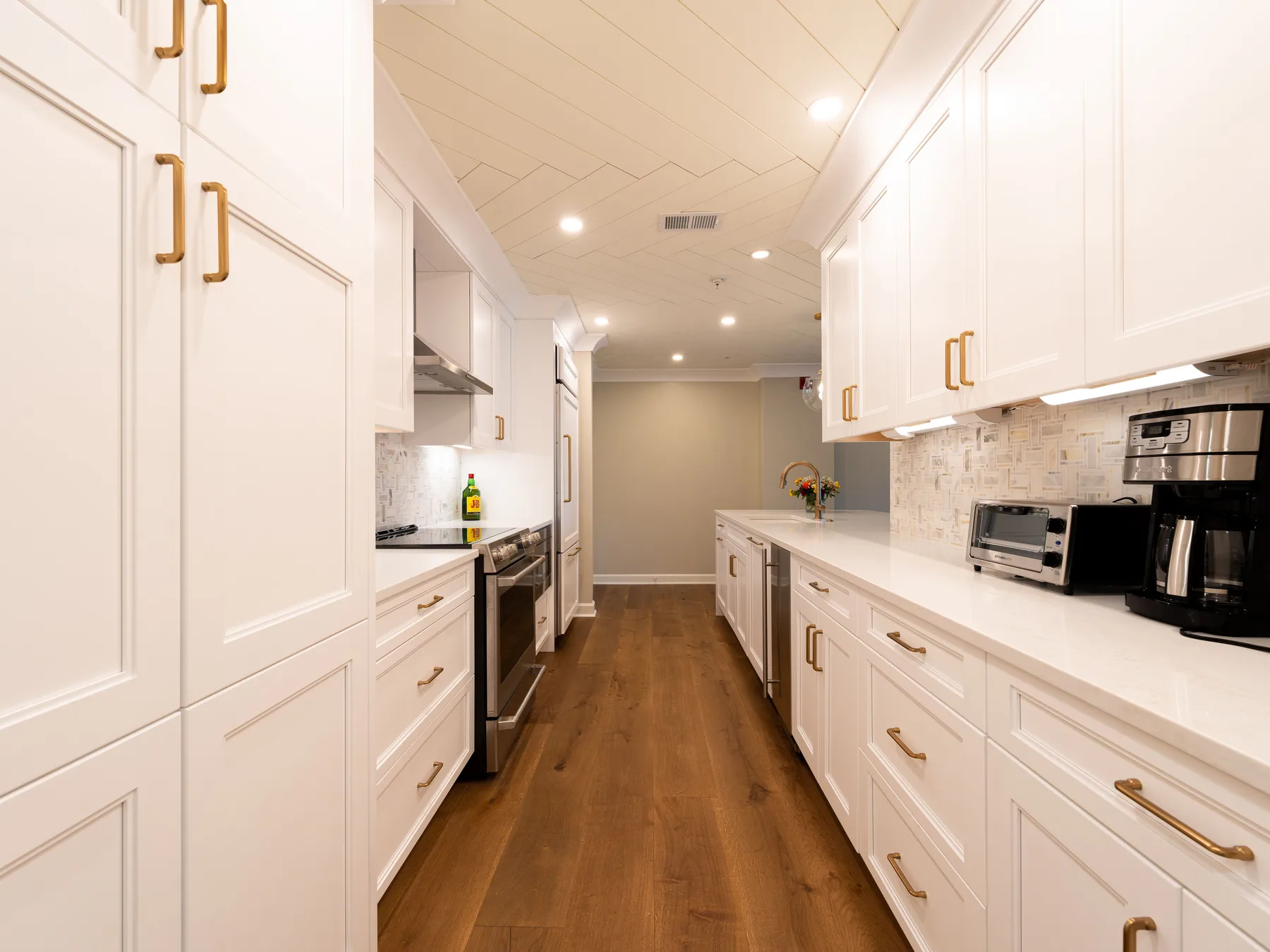A white galley kitchen with brass pulls, a planked ceiling and oak floors